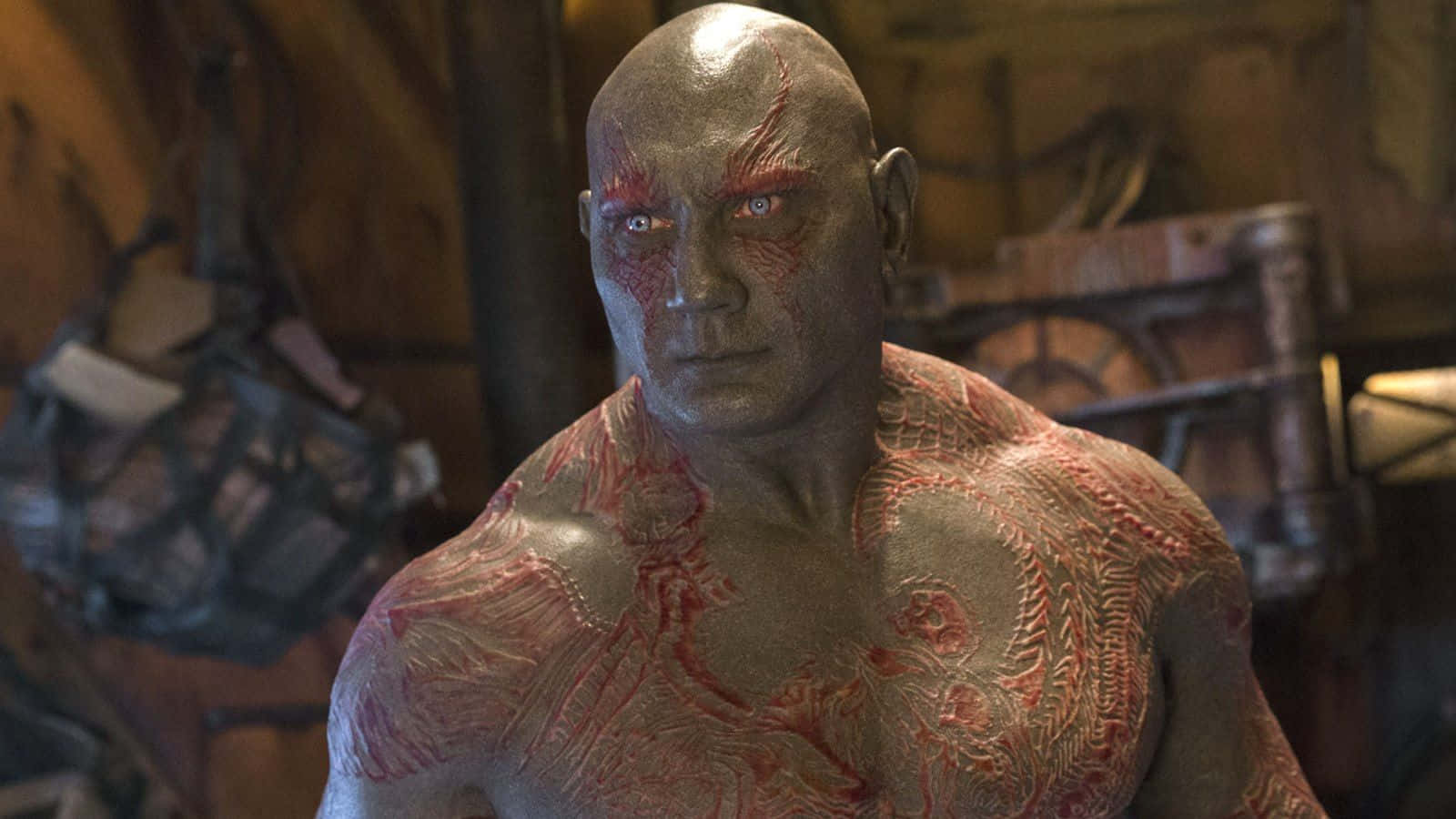 Drax 桌布 壁紙 — 一個肌肉發達、灰色皮膚、帶有紅色標記和銳利眼神的男人在昏暗工作室的特寫。