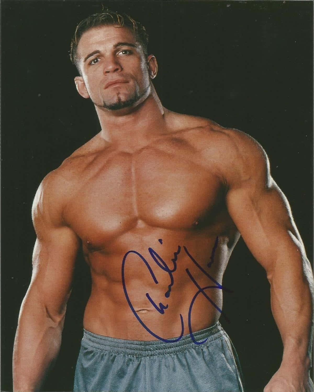 Charlie Haas 桌布 壁紙 — 一個肌肉發達、留著山羊鬍的男人，在黑色背景前凝視鏡頭，腹部有藍色簽名。