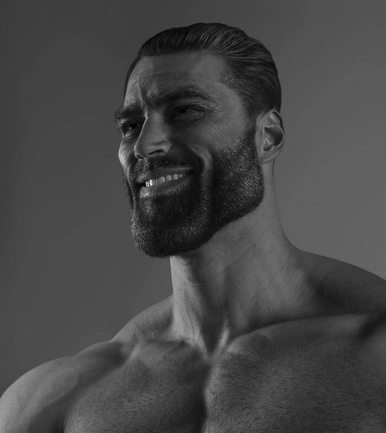 一個留著鬍鬚、肌肉線條分明的男人在黑白工作室肖像中微笑。