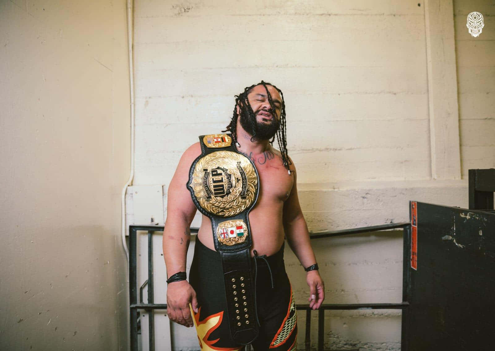 WWE 桌布 壁紙 — 一個肌肉發達、留著辮子的摔角手自信地站在純白牆前，戴著金色冠軍腰帶。