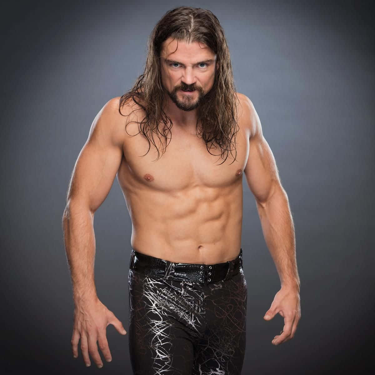 WWE 桌布 壁紙 — 一個肌肉發達、留著黑色長髮和鬍鬚的男人，穿著帶有白色塗鴉的閃亮黑色摔角褲，眼神專注。