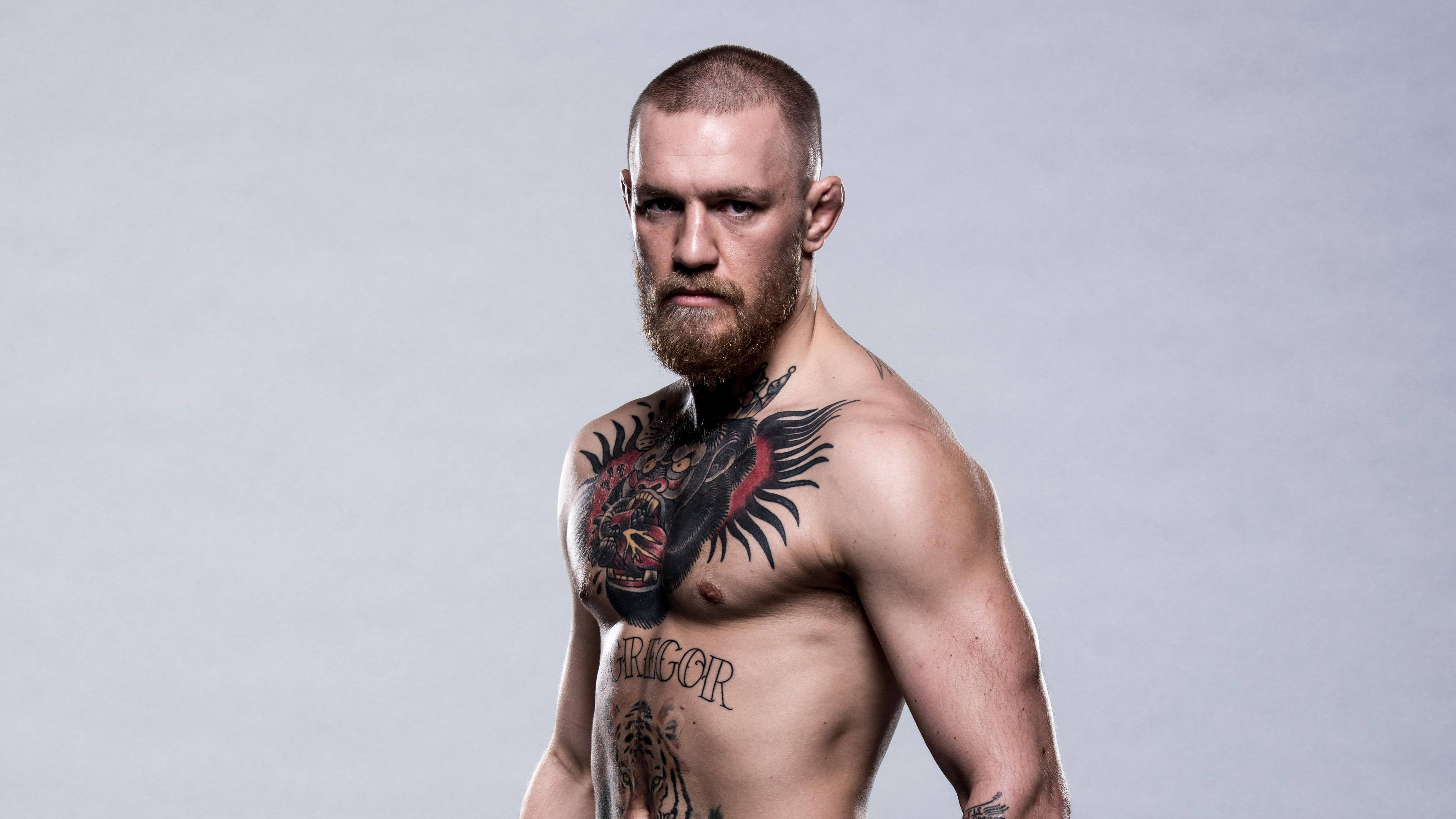 Mcgregor 桌布 壁紙 — 一個肌肉發達、留鬍鬚、有刺青的男人，在純灰色背景前強烈地凝視。
