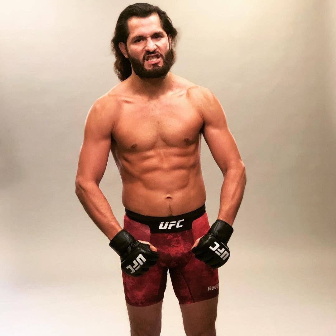 UFC 桌布 壁紙 — 一個肌肉發達、留鬍鬚的男人，穿著UFC短褲和手套，在純色攝影棚背景前擺出挑釁姿勢。