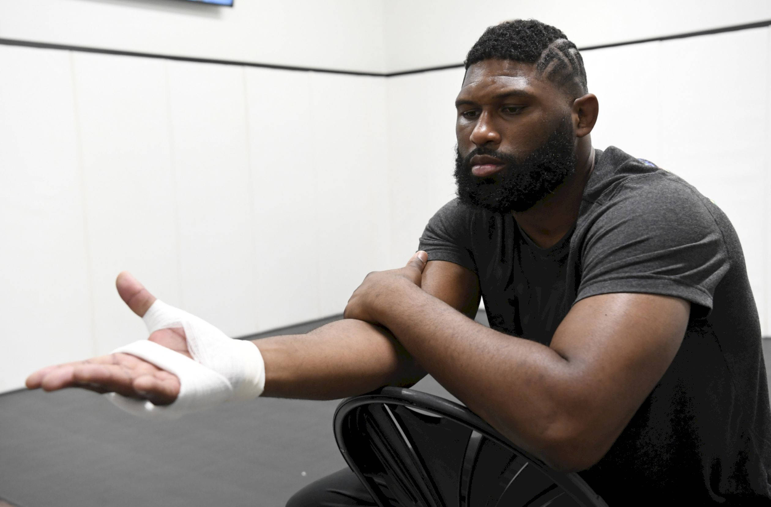 UFC 桌布 壁紙 — 一個肌肉發達、留鬍鬚的男人坐在健身房的黑色椅子上，展示他纏著繃帶的手，表情嚴肅。