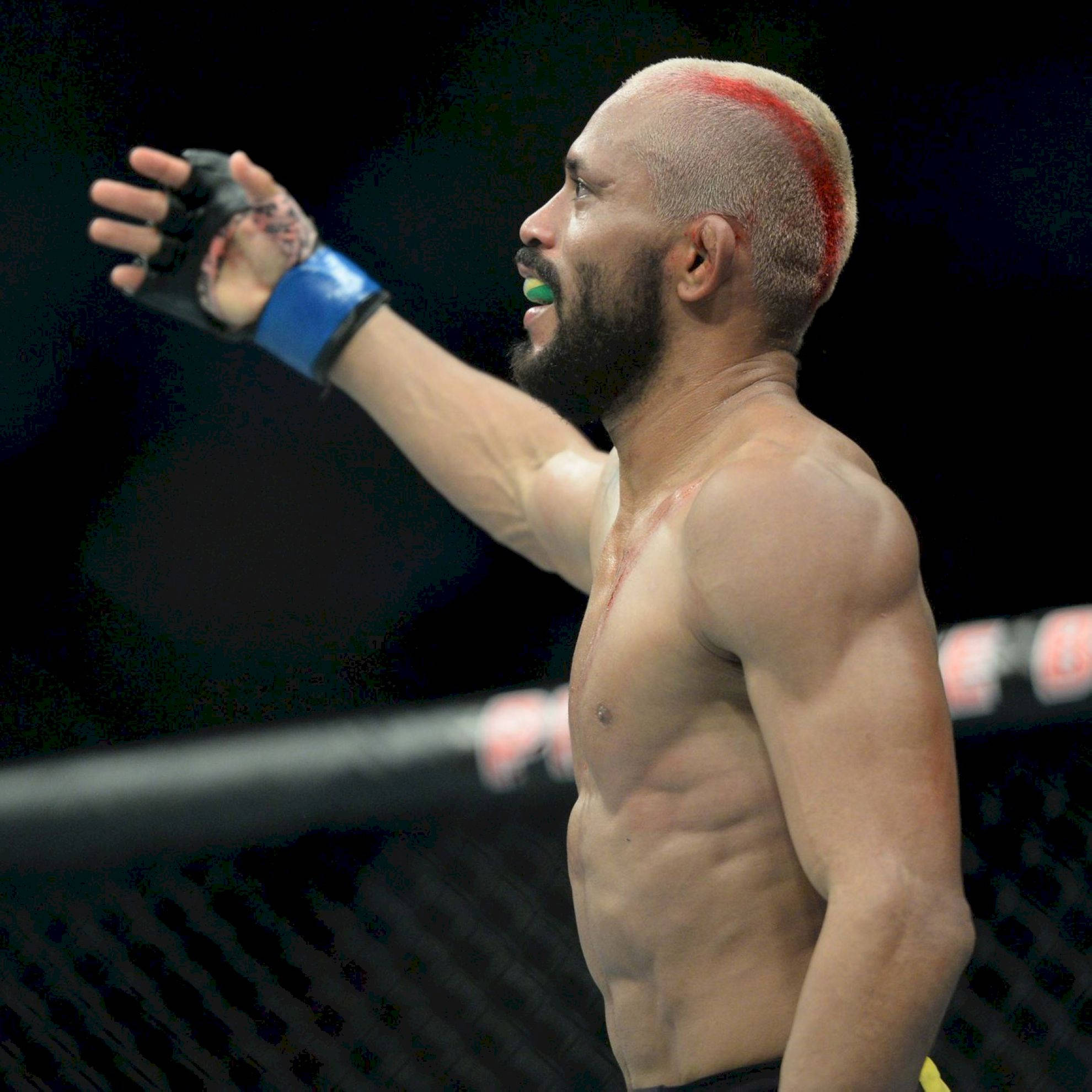 MMA 桌布 壁紙 — 一個肌肉發達、紅色條紋髮型的戰士在黑暗的八角籠內慶祝比賽勝利。