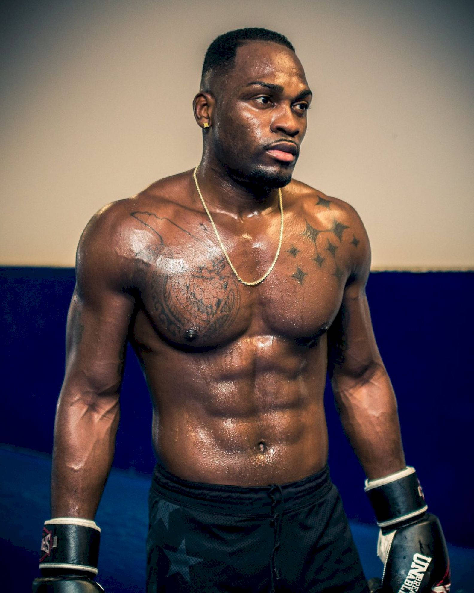 Champion 桌布 壁紙 — 一個肌肉發達、紋身和汗水在攝影棚燈光下閃閃發光的拳擊手，正專注地凝視著鏡頭外。