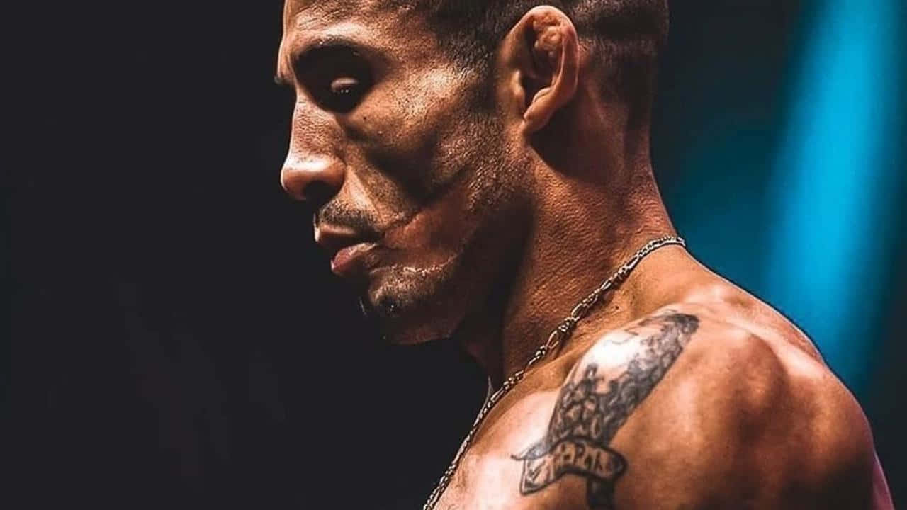 UFC 桌布 壁紙 — 一個肌肉發達、肩膀有刺青、戴著鏈條項鍊的男人，在深藍色背景上側面凝視。