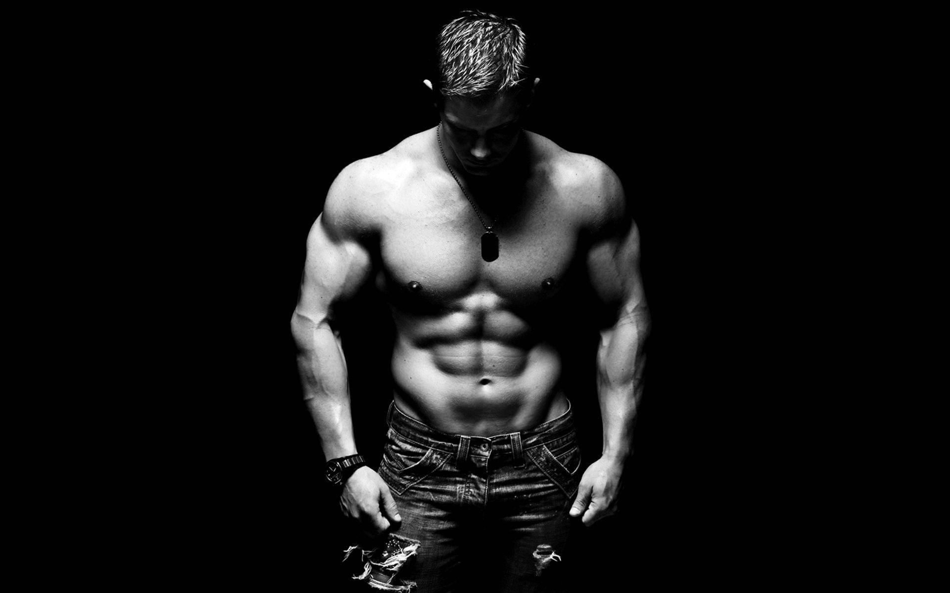 Fitness 桌布 壁紙 — 一個肌肉發達、腹肌線條分明的男人，赤裸上身站在黑色背景前，穿著牛仔褲和狗牌項鍊。