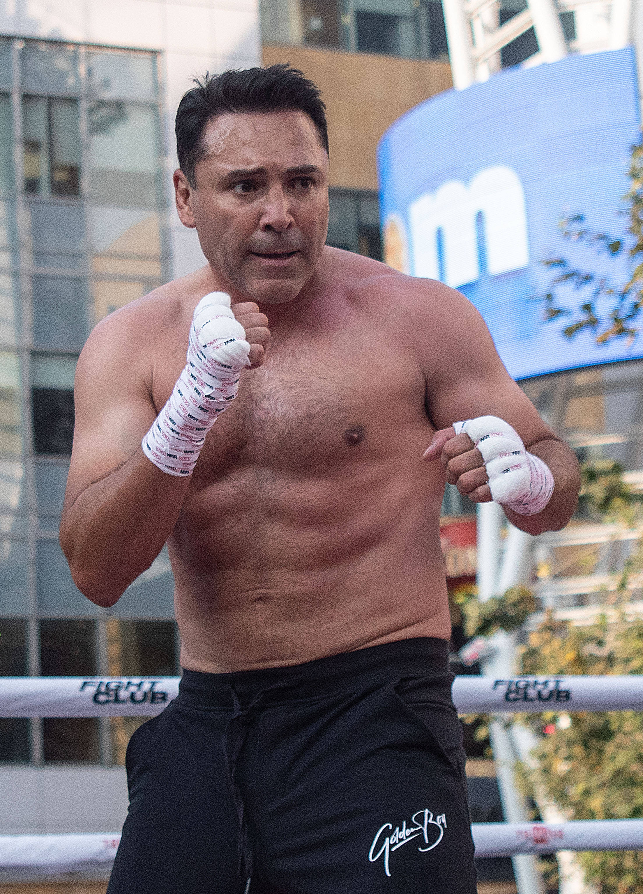 Boxing 桌布 壁紙 — 一個肌肉發達、赤膊上陣、拳頭纏著繃帶的男人，站在戶外拳擊場上，背後是現代建築。