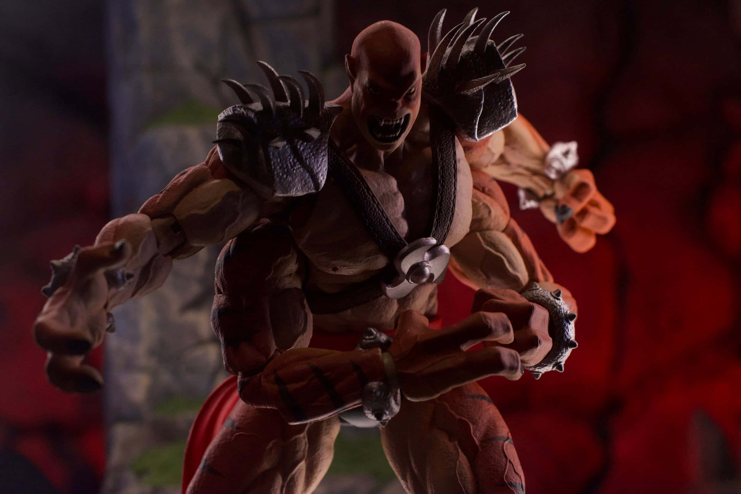 Mortal Kombat Kintaro 桌布 壁紙 — 一個肌肉發達、身穿尖刺盔甲、眼睛發光的惡魔動作人偶，在深紅色背景下擺出侵略性姿勢。