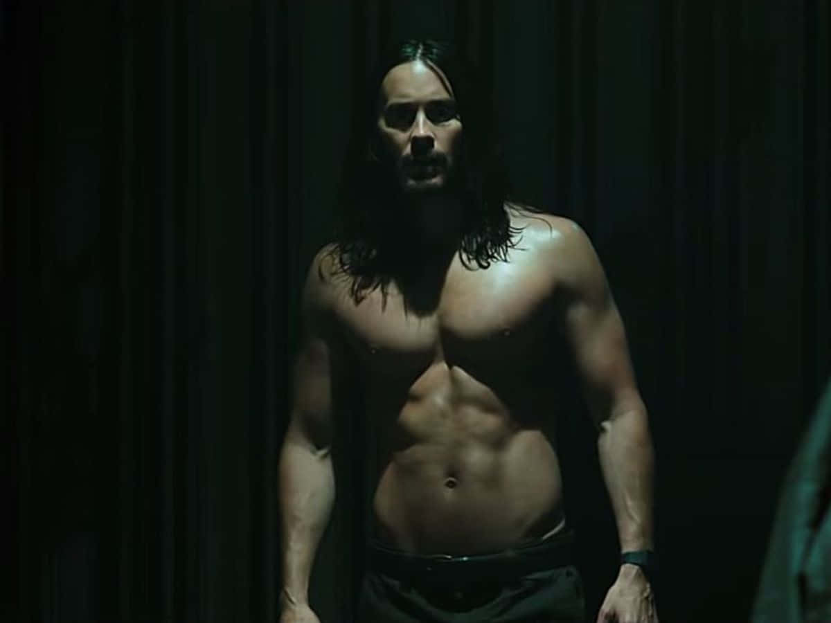 jared leto 桌布 壁紙 — 一個肌肉發達、長黑髮的男人赤裸上身站在昏暗光線中，背景是深色窗簾，他的體格被單一聚光燈突出。