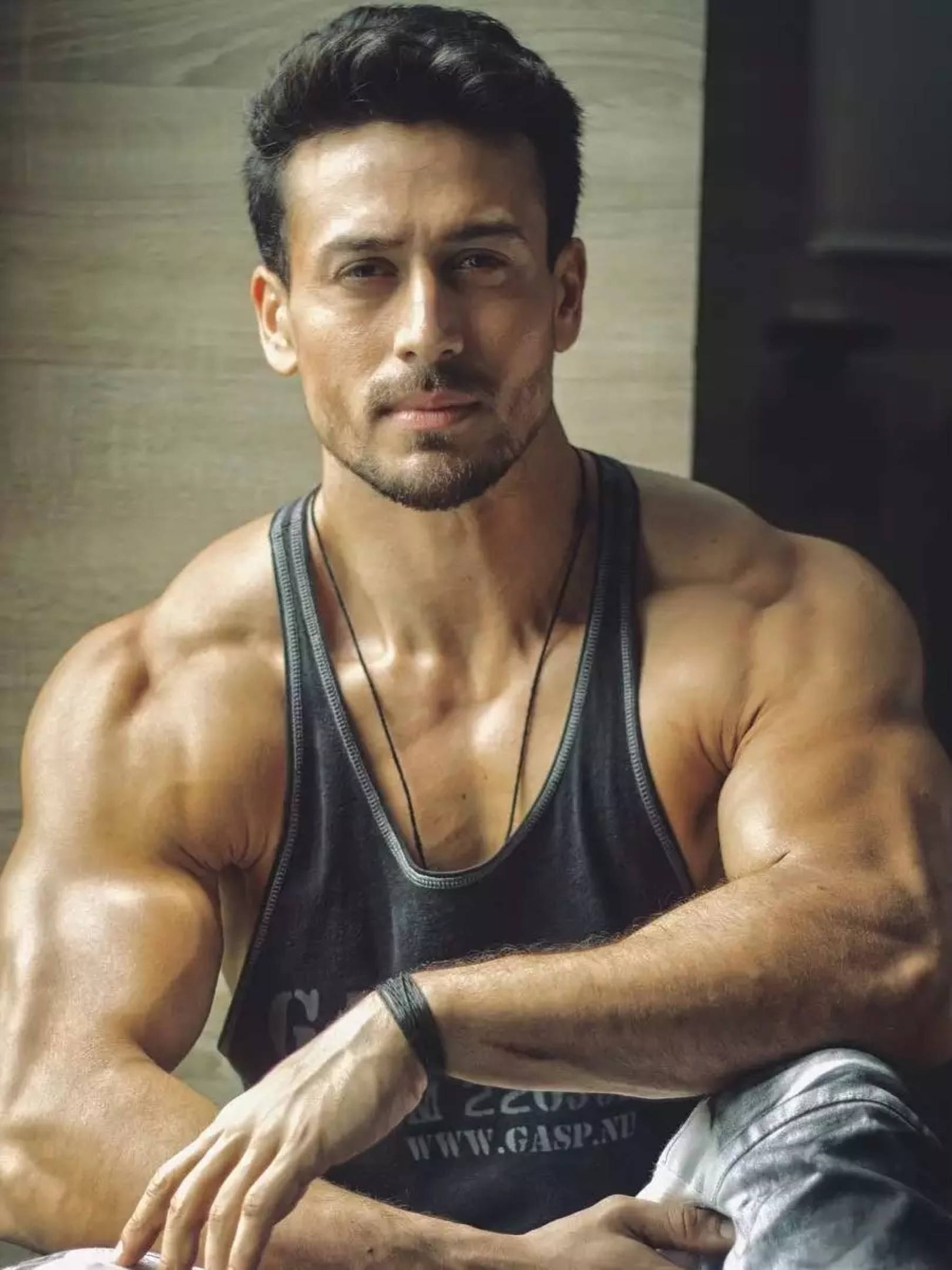 Tiger Shroff 桌布 壁紙 — 一個肌肉發達、黑髮帶鬍渣的男人自信地凝視鏡頭，身穿黑色背心。