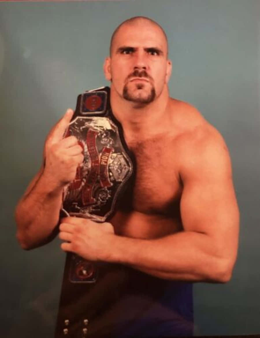 Nikita Koloff 桌布 壁紙 — 一個肌肉發達的光頭摔角手，留著山羊鬍，在純色青綠色攝影棚背景前拿著冠軍腰帶。