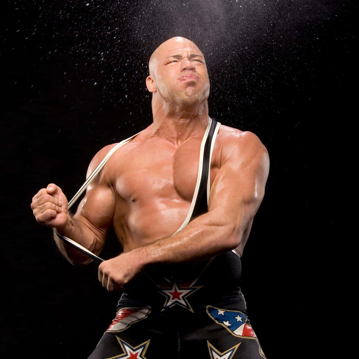 WWE 桌布 壁紙 — 一個肌肉發達的光頭摔角手穿著愛國短褲，在黑色背景下抓住肩帶向上噴水。