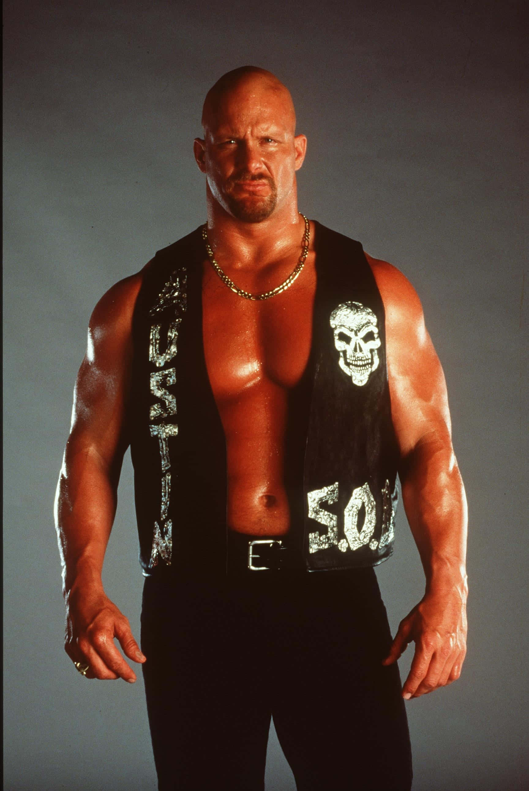WWE 桌布 壁紙 — 一個肌肉發達的光頭男人，身穿帶有骷髏頭和「5.0」補丁的黑色背心，自信地站在灰色攝影棚背景前。