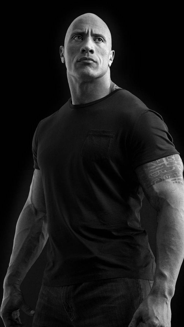 The Rock 桌布 壁紙 — 一個肌肉發達的光頭男人穿著黑色T恤，在純黑背景下強烈地向上凝視。