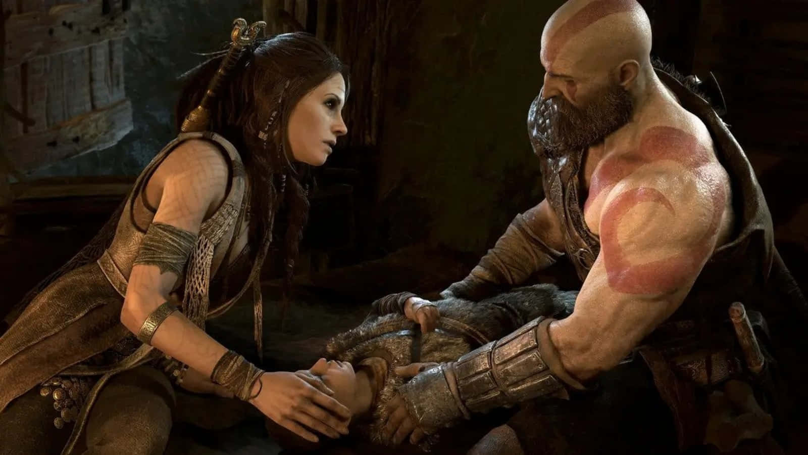 God Of War Characters 桌布 壁紙 — 一個肌肉發達的光頭男子，身上有紅色紋身和鬍鬚，跪在一個身穿盔甲的女人旁邊，他們在一個光線昏暗的石室裡一起抱著一個孩子。