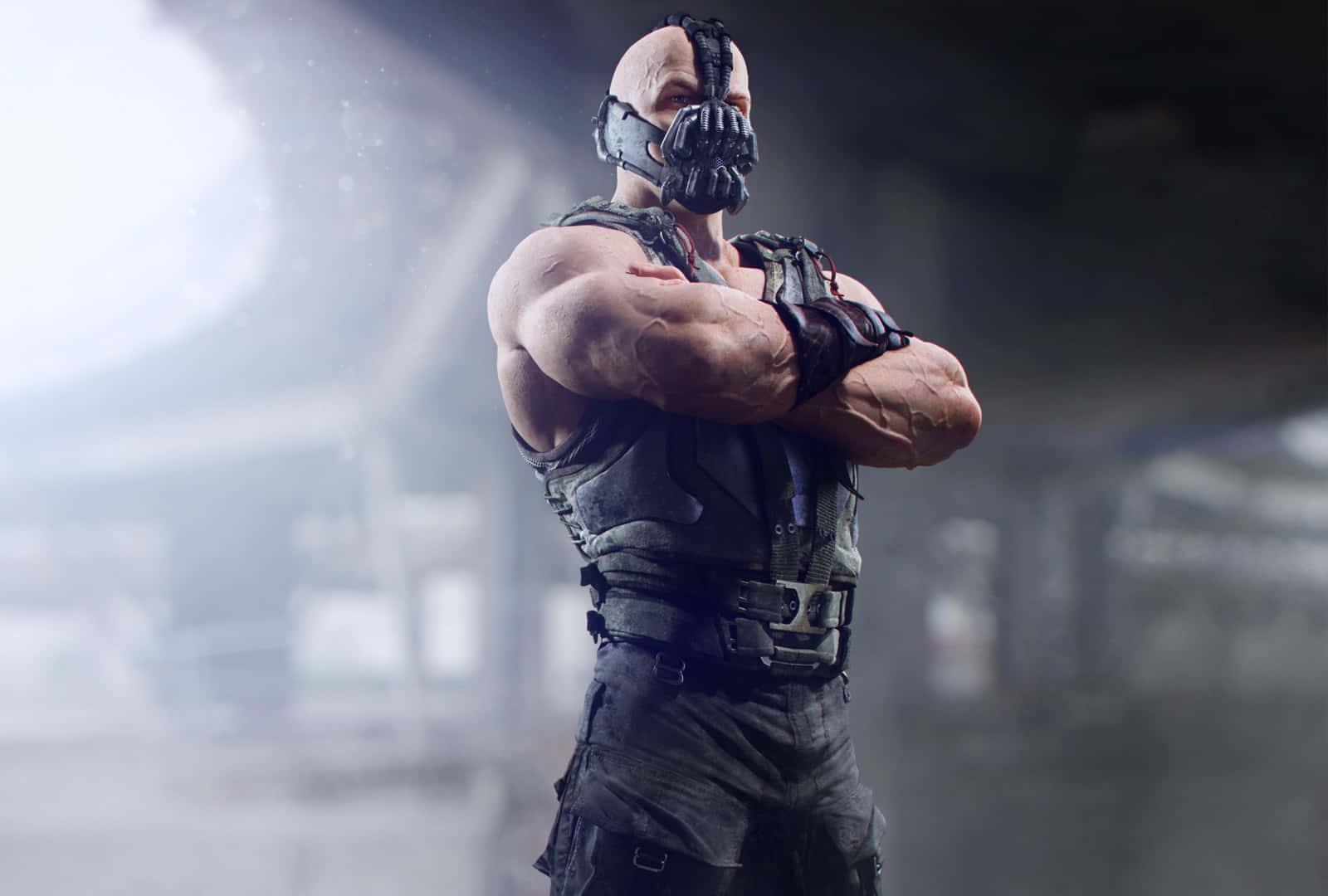 bane 桌布 壁紙 — 一個肌肉發達的光頭男子，身穿黑色裝甲服和蝙蝠面具，在煙霧瀰漫的工業環境中交叉雙臂站立。