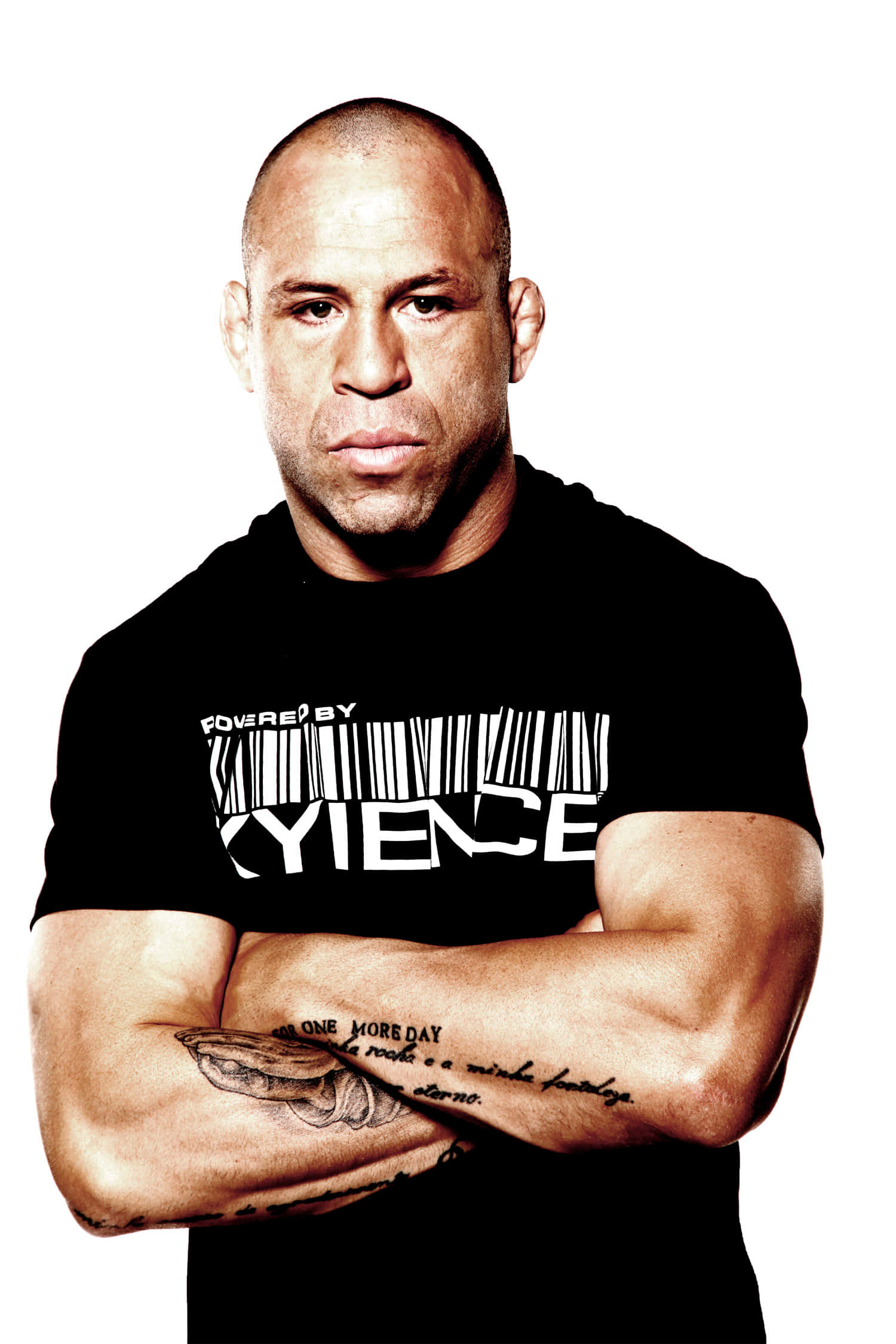 UFC 桌布 壁紙 — 一個肌肉發達的光頭男子交叉雙臂，穿著帶有條碼標誌的黑色T恤，背景是純白色。