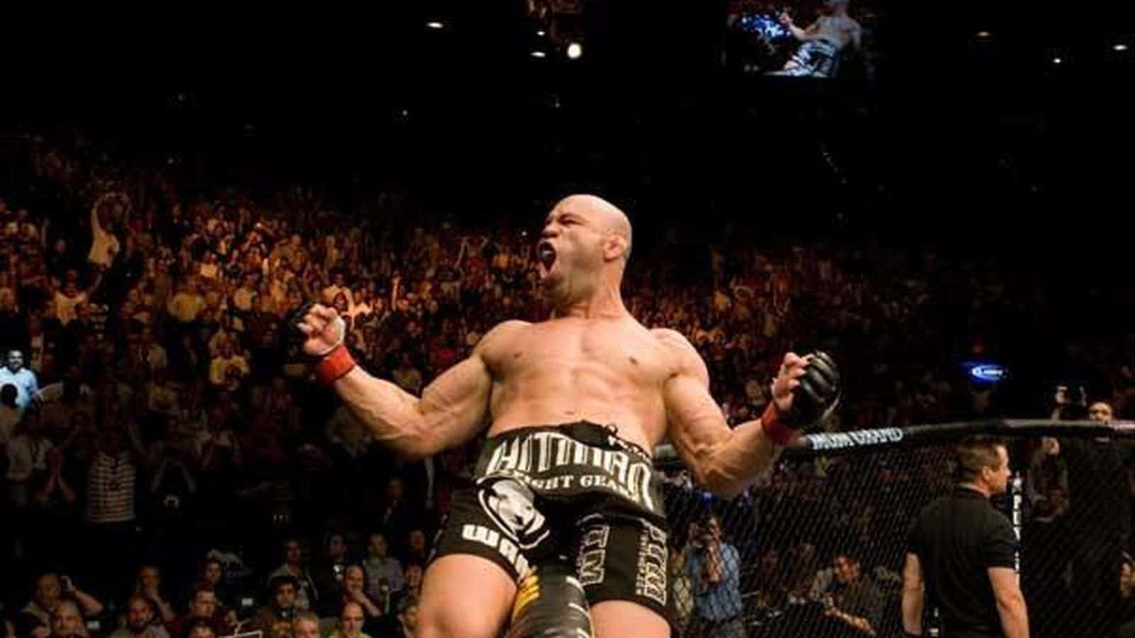 UFC 桌布 壁紙 — 一個肌肉發達的光頭鬥士在籠內勝利咆哮，身後是歡呼的人群擠滿了競技場。