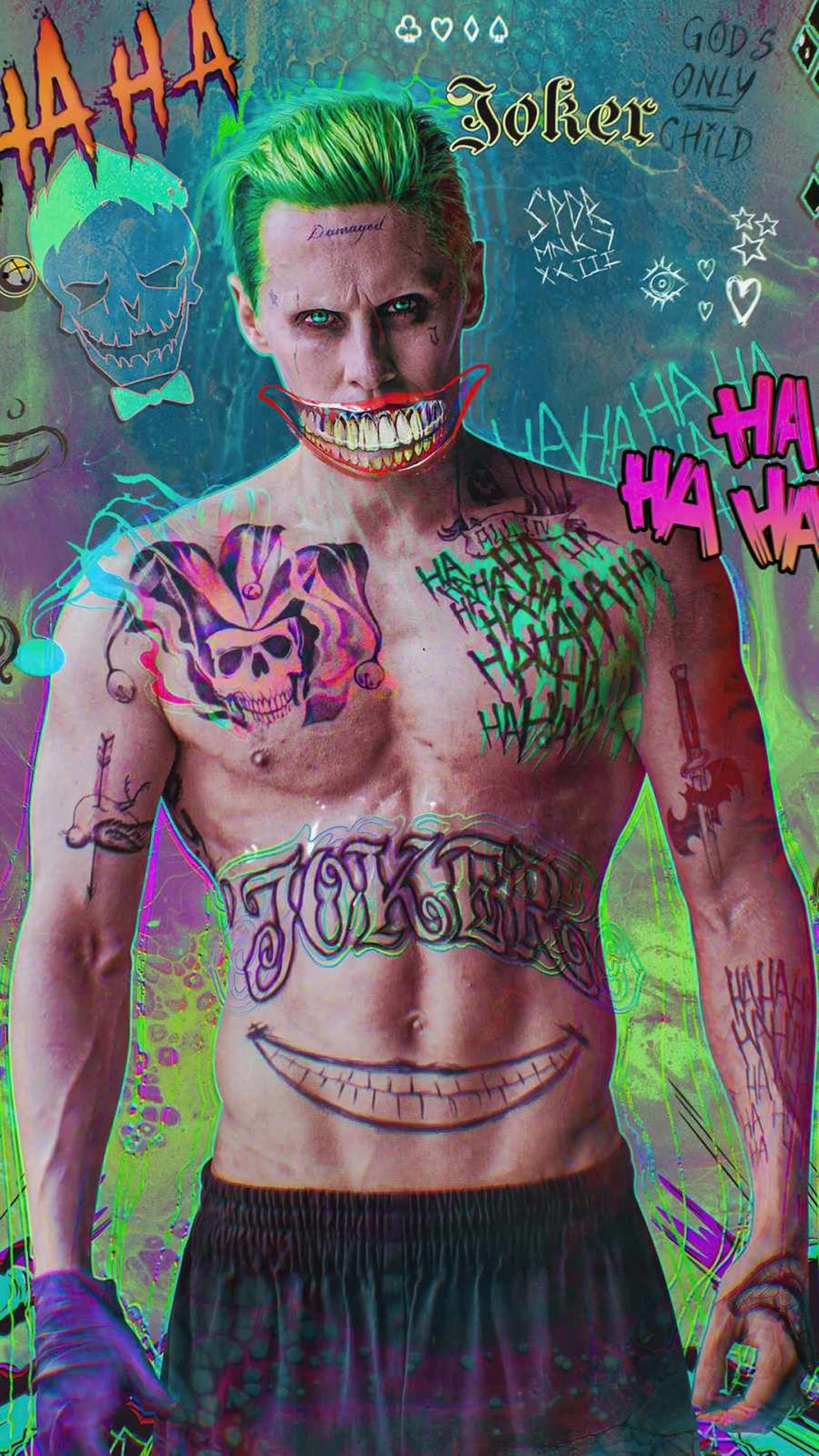 Joker 2019 桌布 壁紙 — 一個肌肉發達的小丑，綠色頭髮和刺青，站在一面充滿塗鴉的牆前，牆上滿是混亂的符號和笑聲。