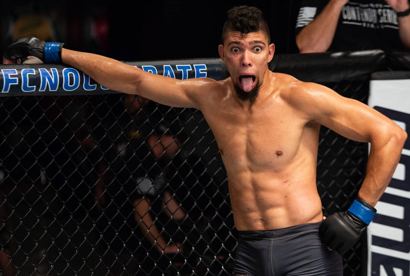 MMA 桌布 壁紙 — 一個肌肉發達的戰士伸出長舌頭，在MMA八角籠內瘋狂慶祝。