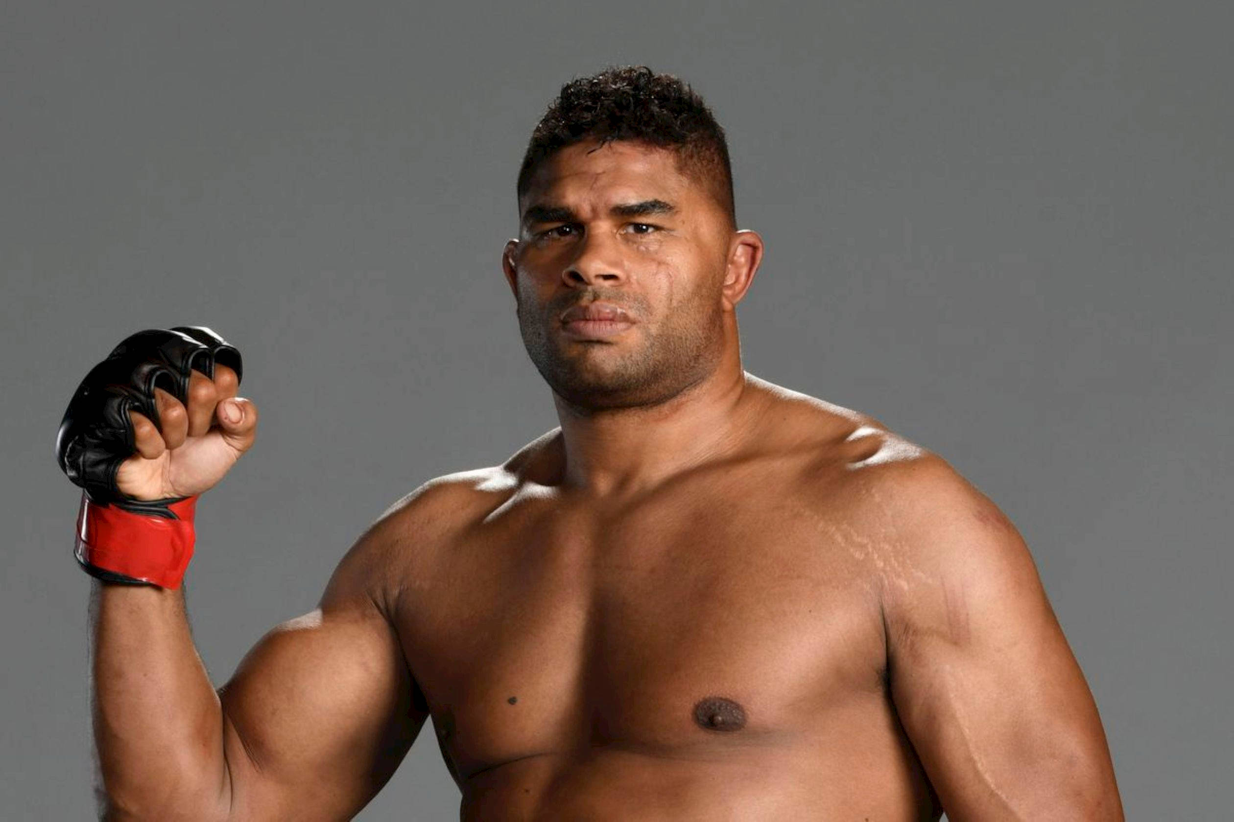 UFC 桌布 壁紙 — 一個肌肉發達的戰士戴著紅色和黑色手套，在灰色工作室背景前舉起拳頭，眼神銳利。