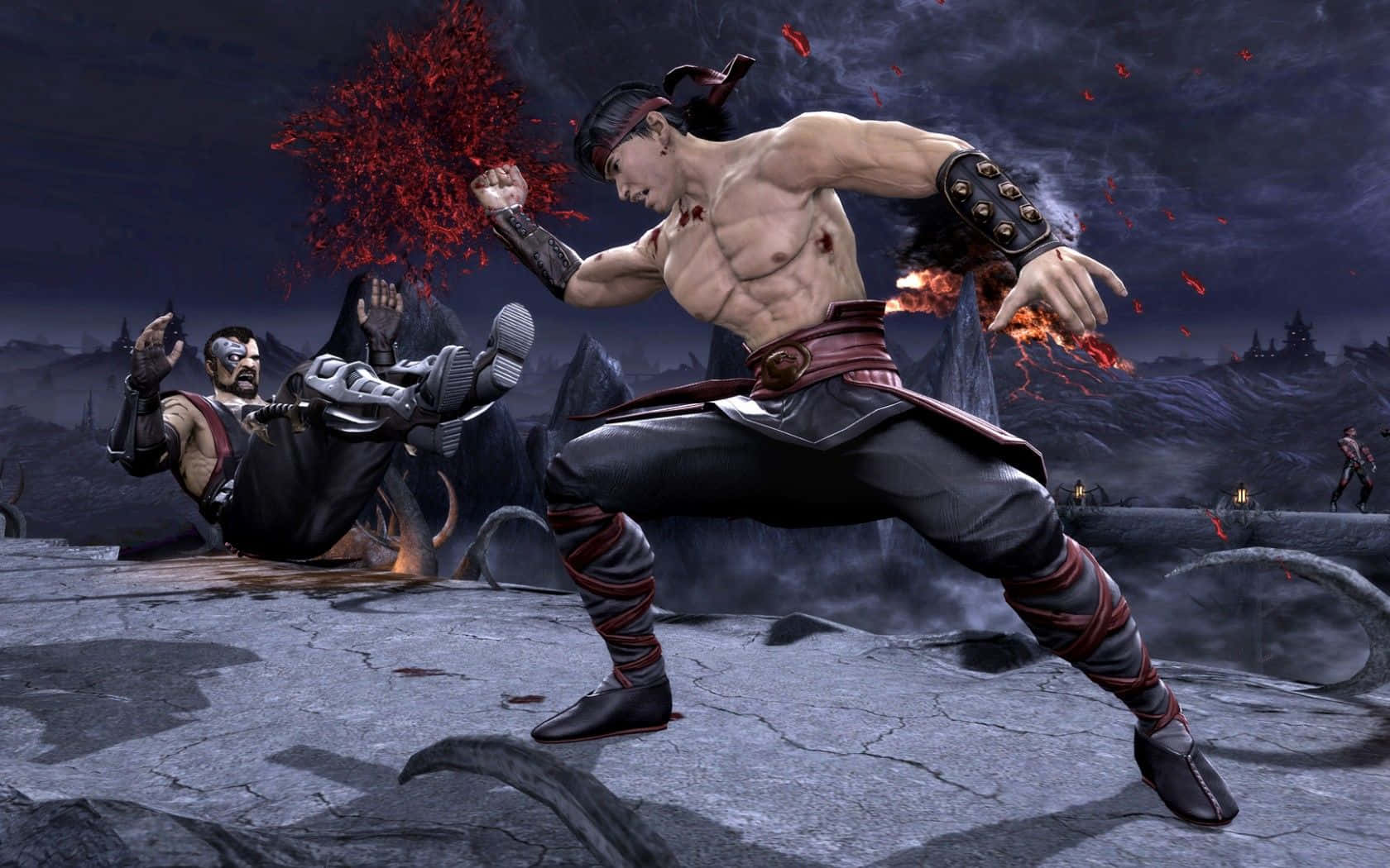 Mortal Kombat Liu Kang 桌布 壁紙 — 一個肌肉發達的戰士穿著黑色和紅色的裝備，在一個黑暗的火山戰場上，向對手踢出強力一腳，周圍有紅色碎片飛舞。