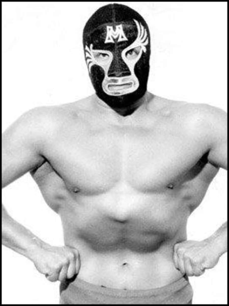 Mask 桌布 壁紙 — 一個肌肉發達的摔角手，戴著黑白面具，上面有「M」標誌，雙手叉腰，自信地站在純色背景前。