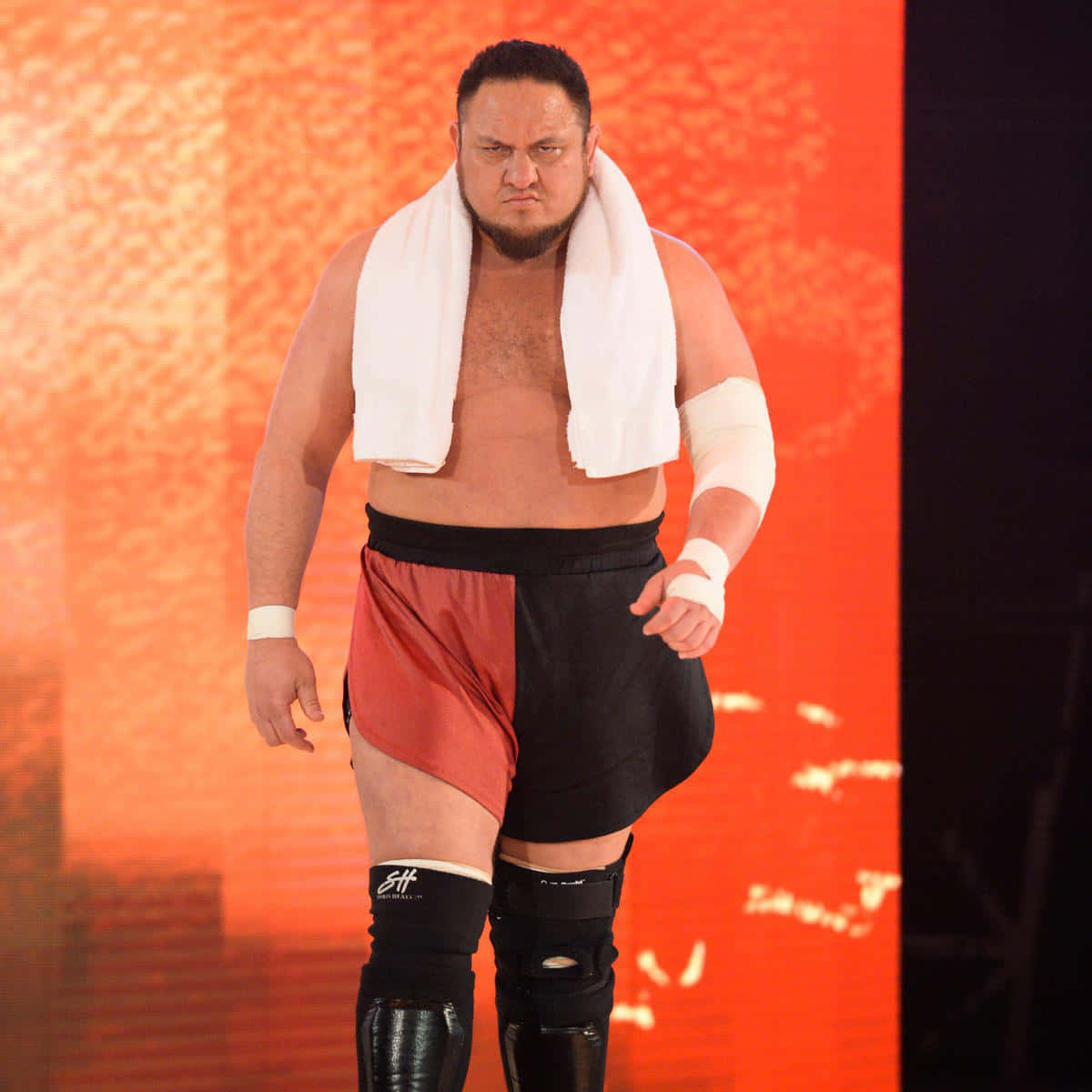 WWE 桌布 壁紙 — 一個肌肉發達的摔角手，肩上披著白色毛巾，在發光的橙色背景下帶著兇猛的表情向前邁進。