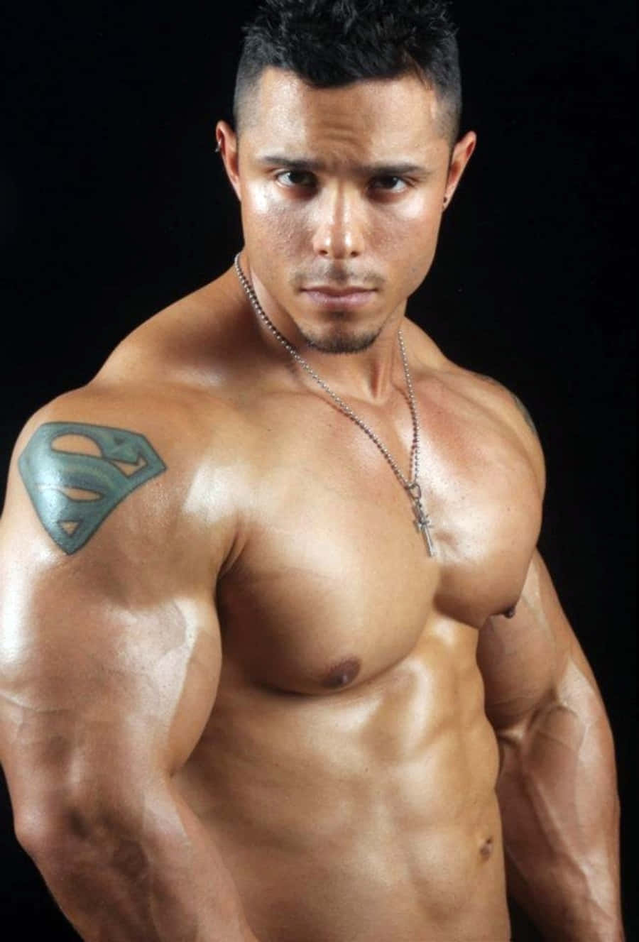 Muscle 桌布 壁紙 — 一個肌肉發達的男人，肩膀上有一個超人刺青，在黑色背景前強烈地凝視。