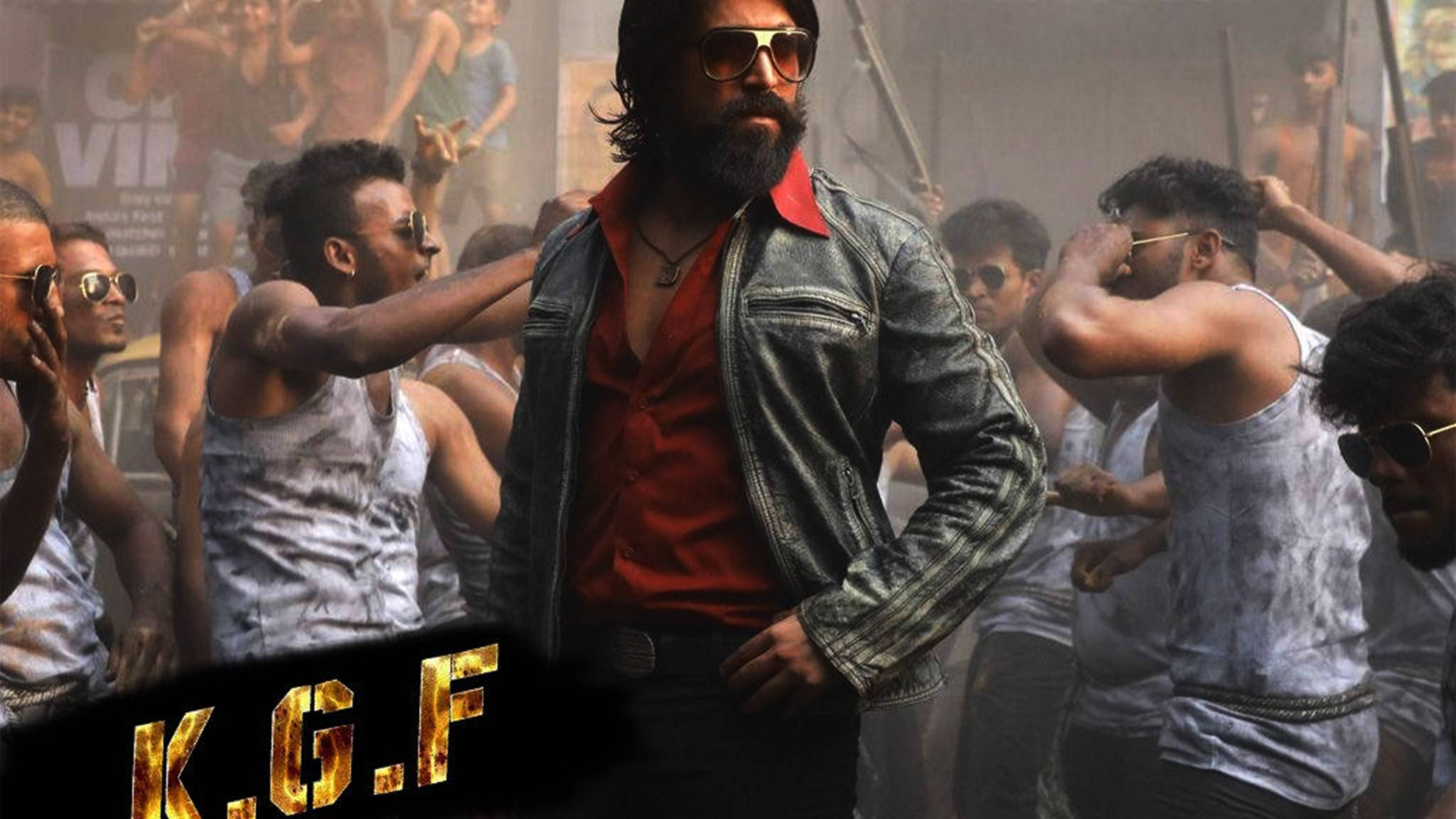 kgf 4K 桌布 壁紙 — 一個肌肉發達的男人，身穿紅色襯衫和皮夾克，自信地站在一群赤裸上身的男人中間，背景是粗獷的城市環境。