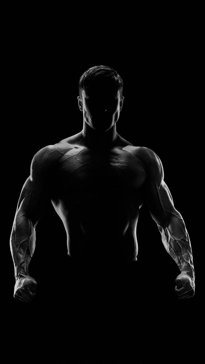 Exercise 桌布 壁紙 — 一個肌肉發達的男人以剪影姿態站在黑色背景前，戲劇性的燈光突顯了他分明的體格。