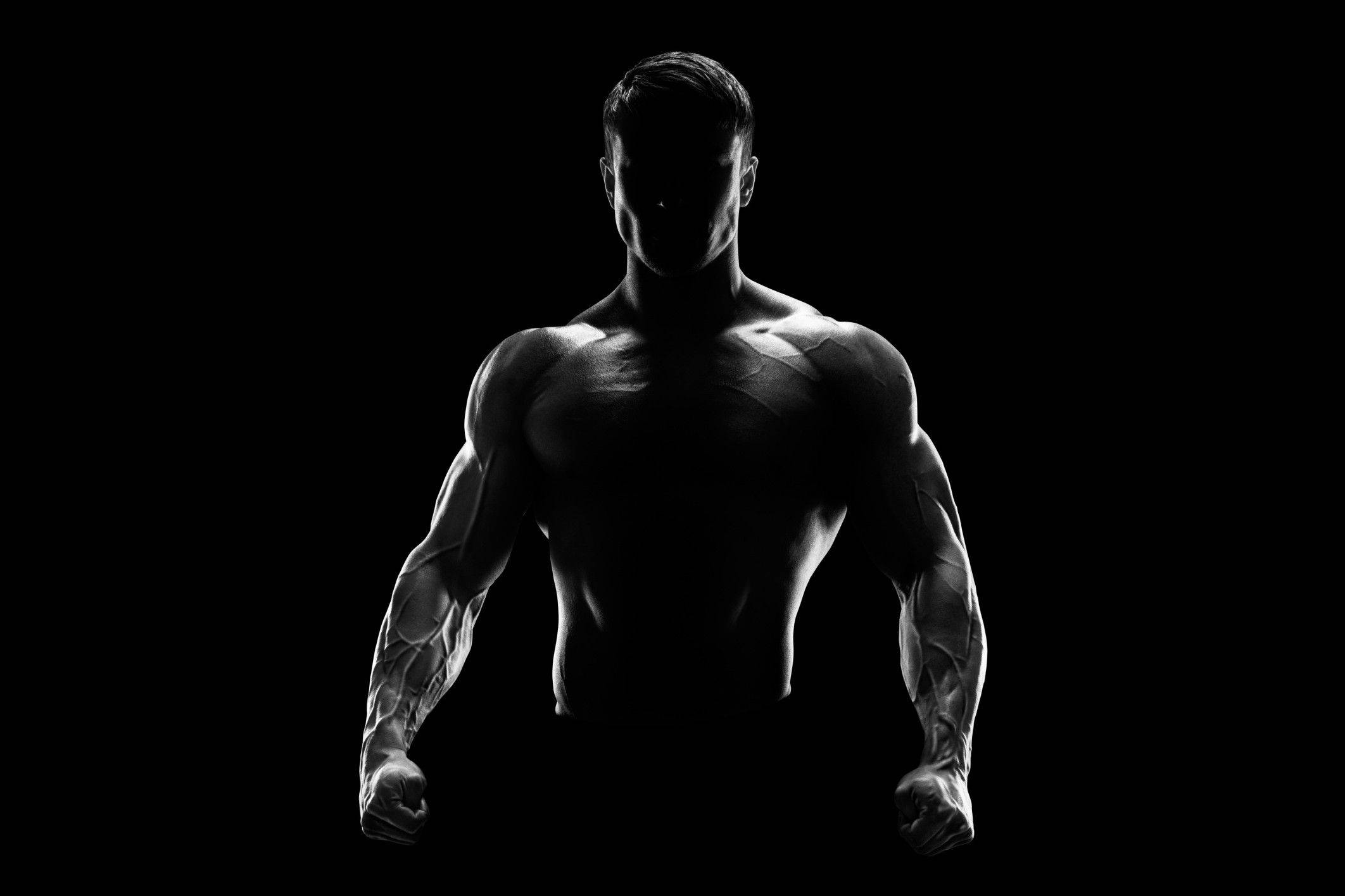 Fitness 桌布 壁紙 — 一個肌肉發達的男人以剪影站在黑色背景前，戲劇性的燈光突顯他線條分明的體格。