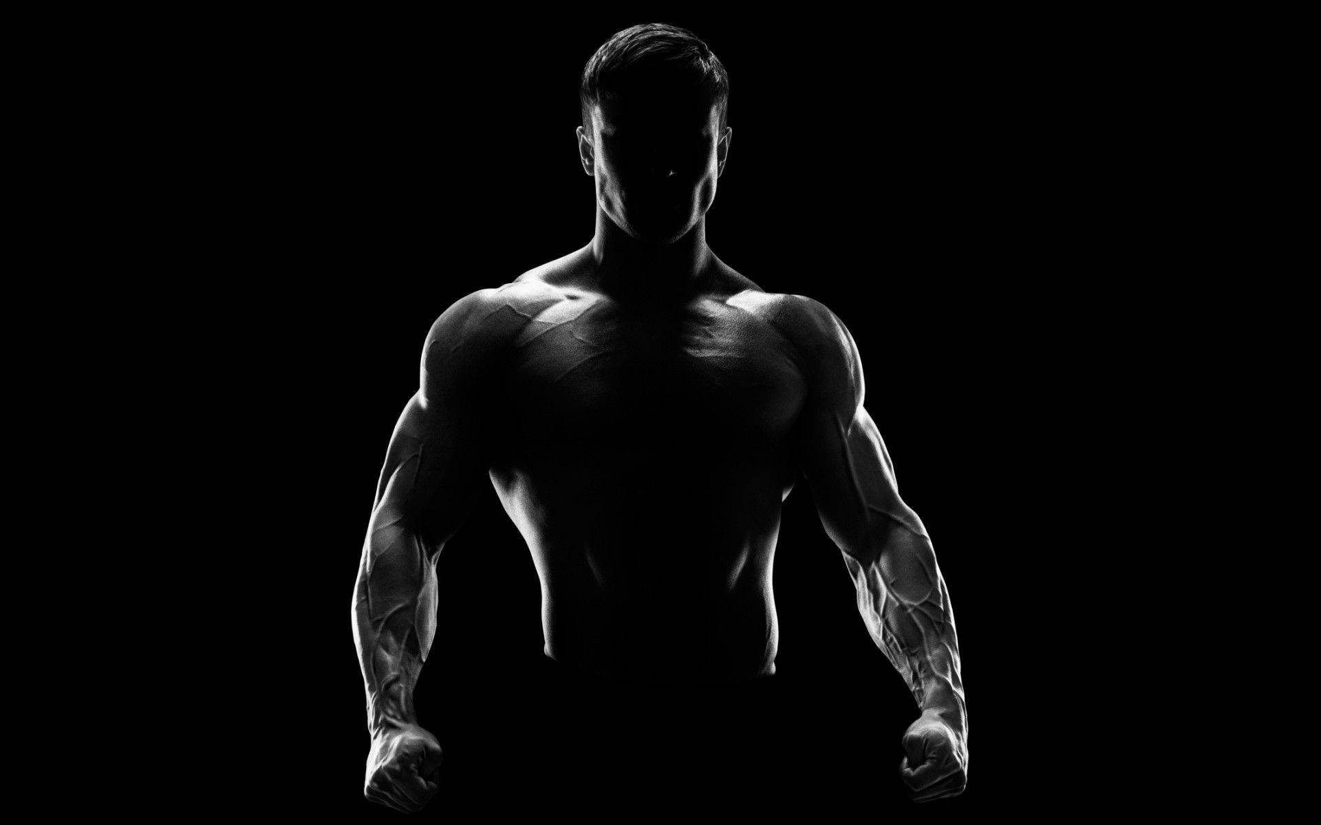 Fitness 桌布 壁紙 — 一個肌肉發達的男人以剪影站在黑色背景前，戲劇性的燈光突顯他清晰的體格。