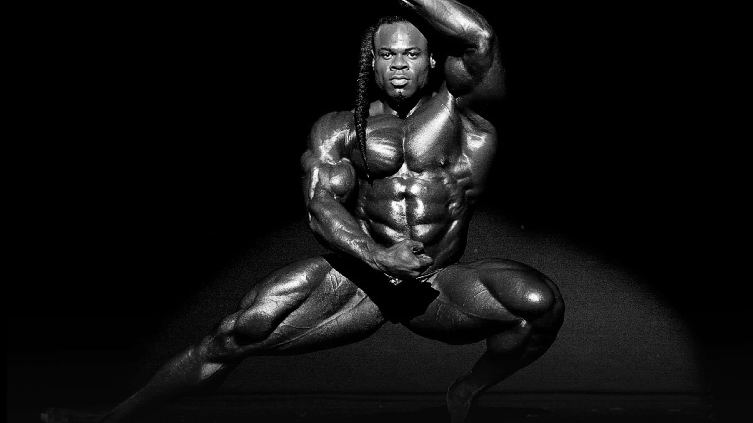 運動 桌布 壁紙 — 一個肌肉發達的男人以戲劇性的黑白姿勢，在深色背景下突顯其清晰的體格。