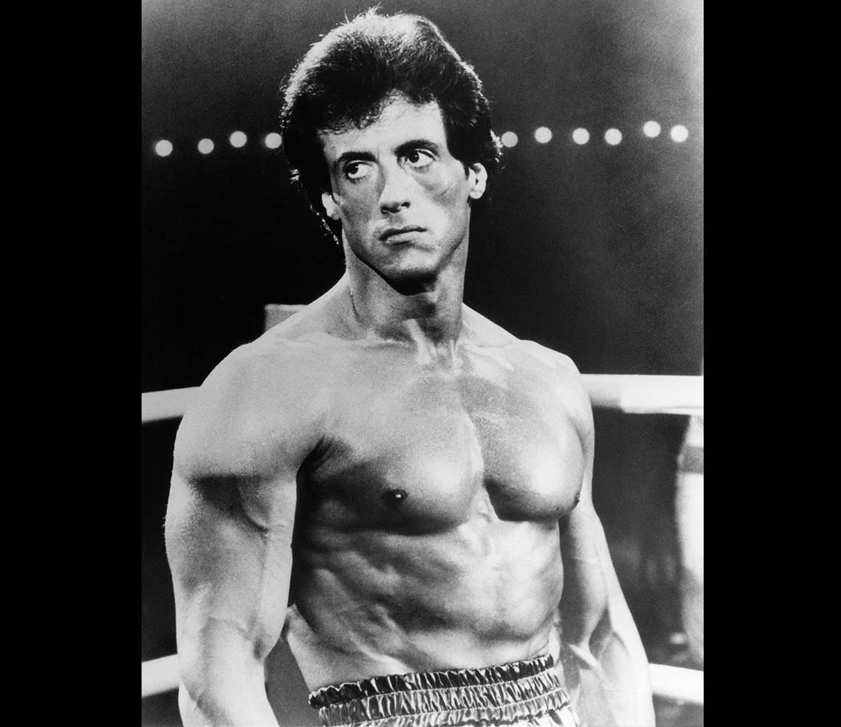 rocky 桌布 壁紙 — 一個肌肉發達的男人在明亮的燈光下赤裸上身站在拳擊台上，表情專注而強烈。