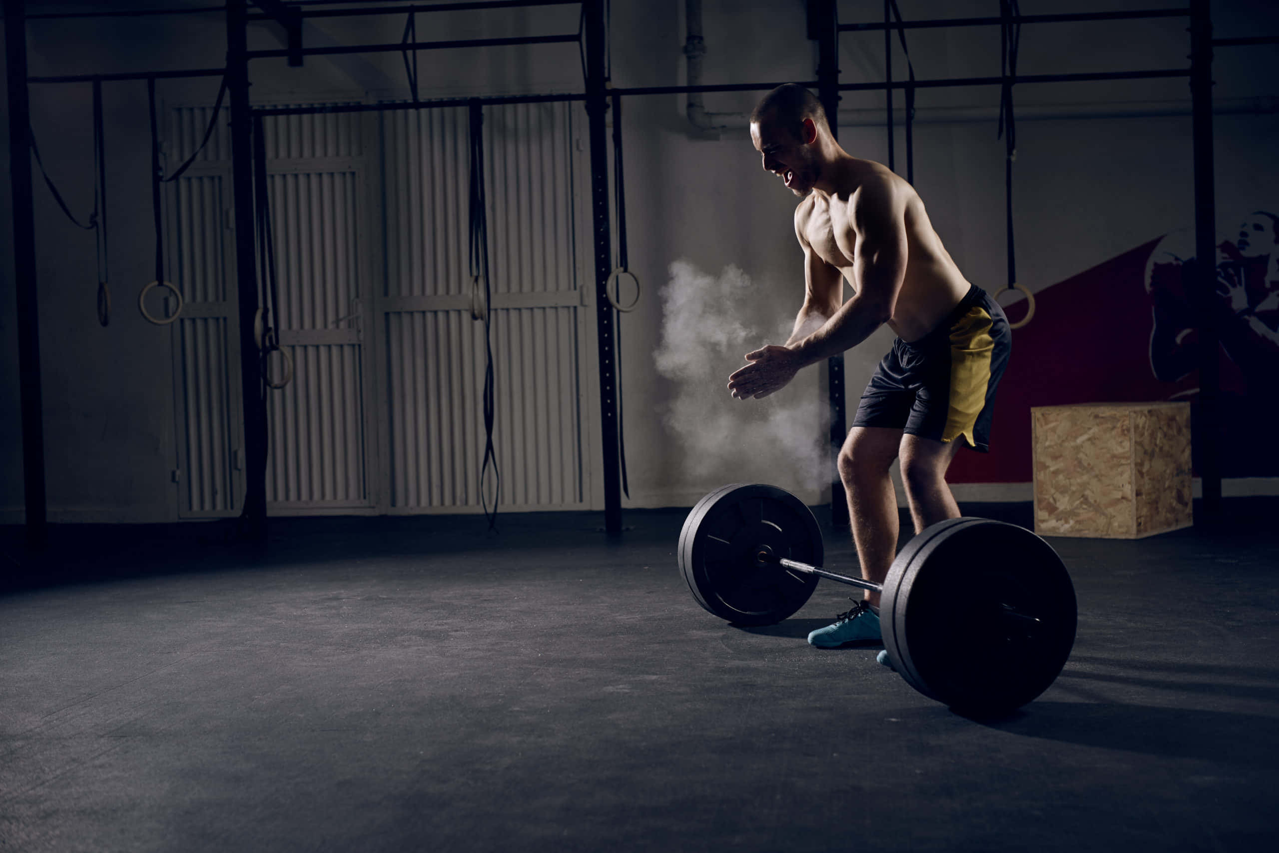 Fitness 桌布 壁紙 — 一個肌肉發達的男人在昏暗的健身房裡，在舉起沉重的槓鈴前，專注地為雙手撲粉。