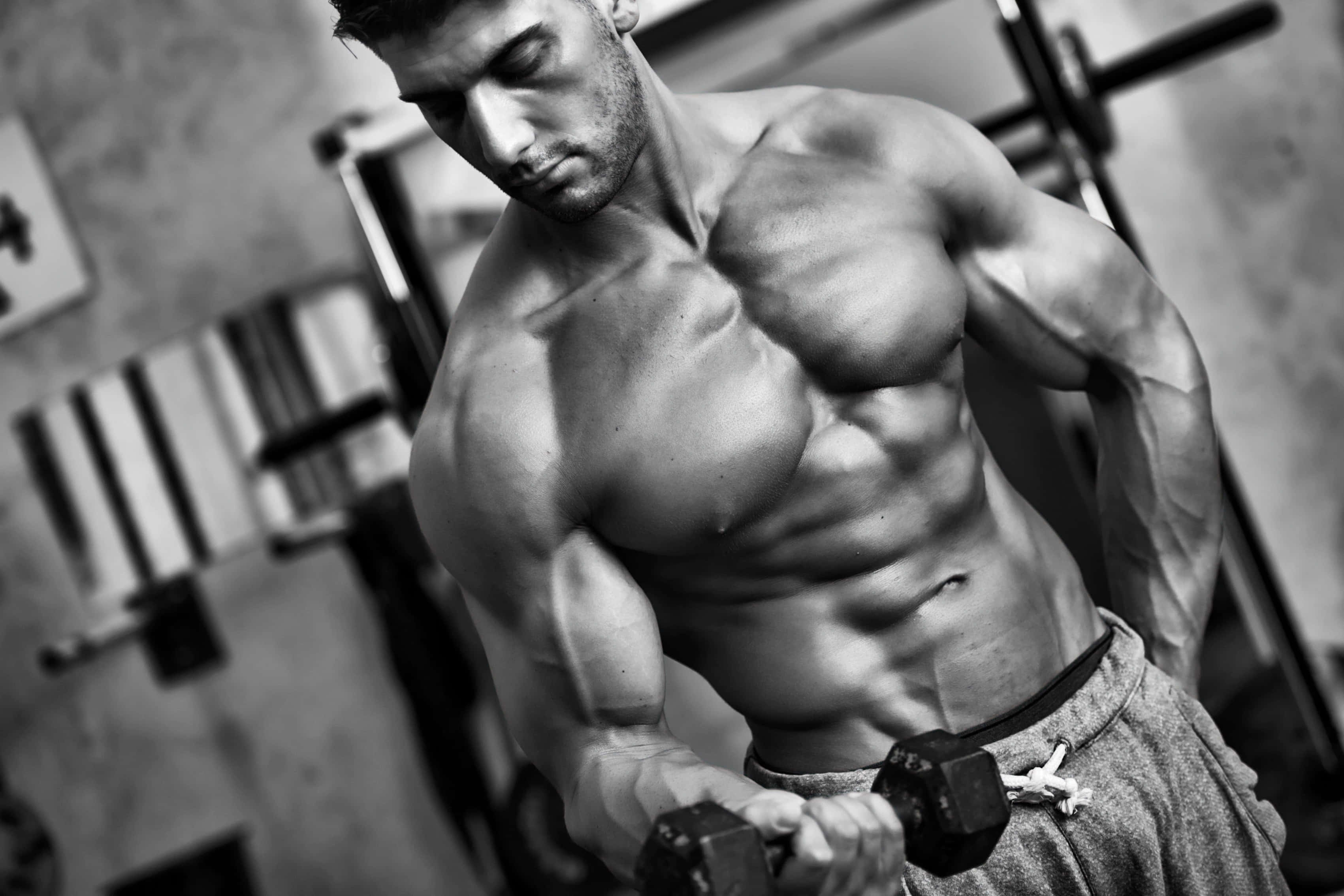 bodybuilding 桌布 壁紙 — 一個肌肉發達的男人在粗獷的健身房中激烈地舉起啞鈴，以戲劇性的黑白畫面捕捉。