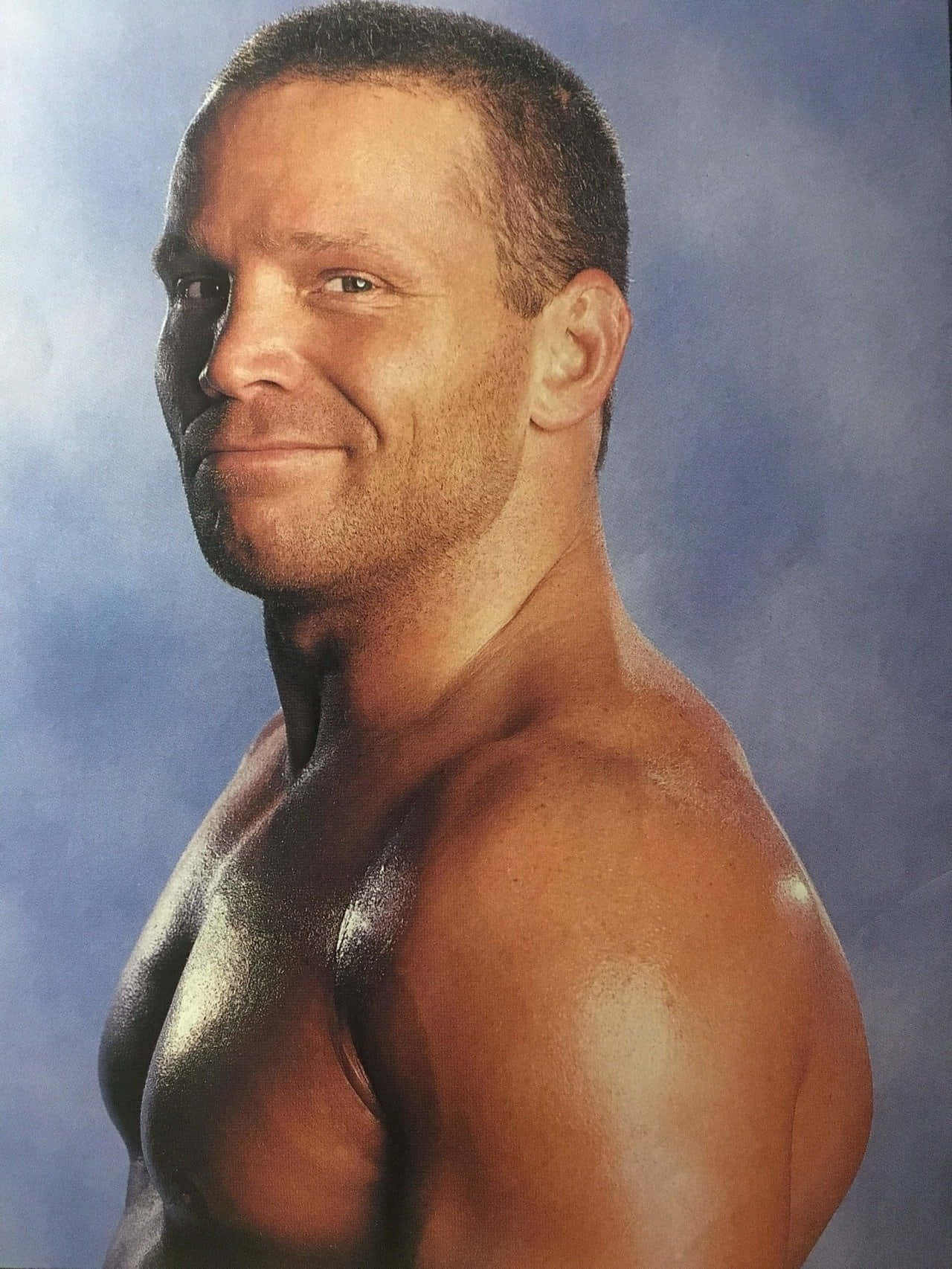 Crash Holly 桌布 壁紙 — 一個肌肉發達的男人帶著自信的假笑，在煙霧藍色背景前的攝影棚燈光下閃耀。