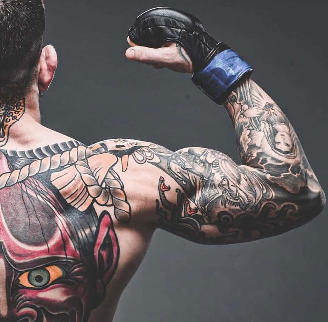 Tattoo 桌布 壁紙 — 一個肌肉發達的男人彎曲他帶有刺青的手臂，展示背上和袖子上複雜的黑紅魔鬼面具圖案。