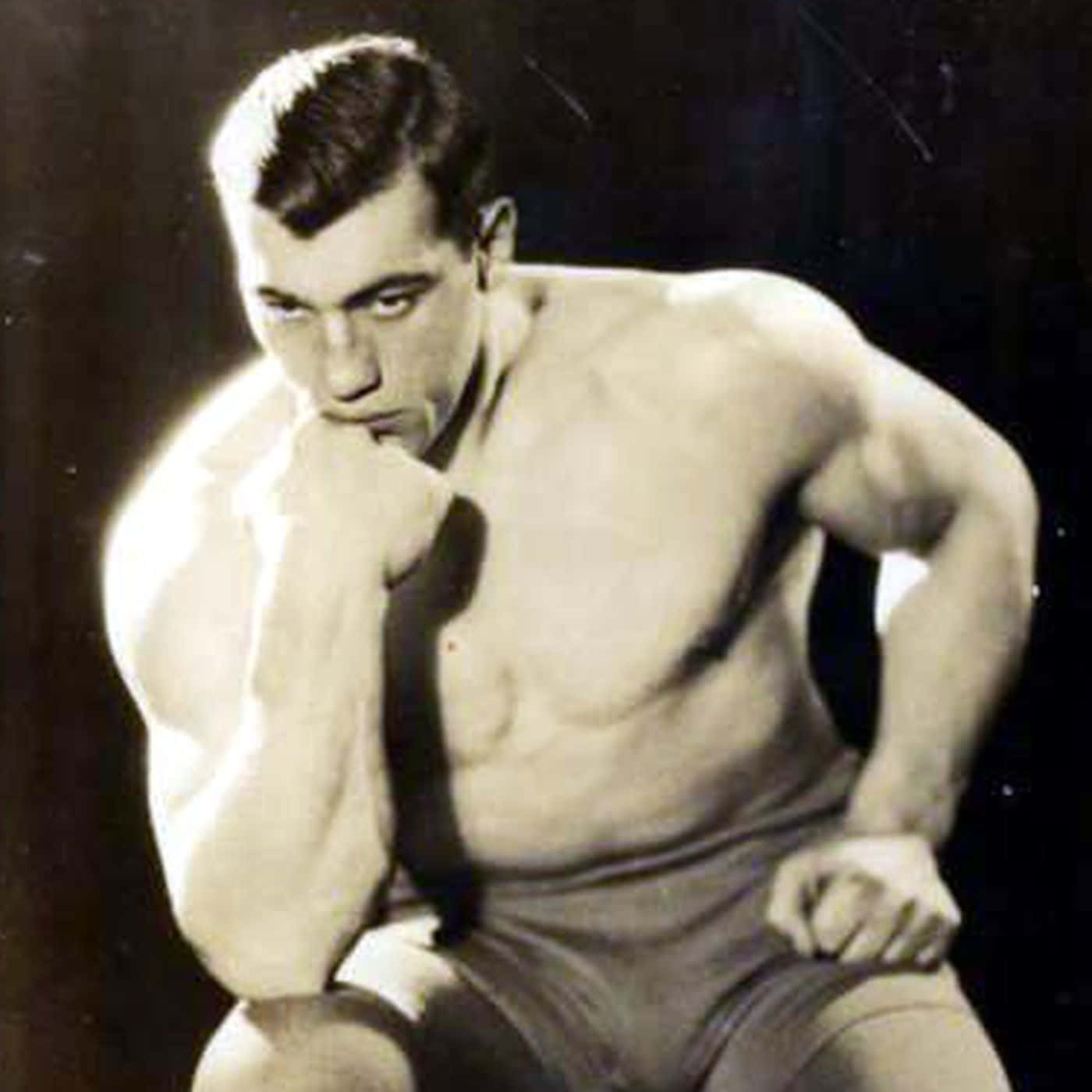 Boxing 桌布 壁紙 — 一個肌肉發達的男人穿著復古摔角褲，在黑暗背景下，一隻拳頭靠近嘴巴，激烈地蹲伏著。