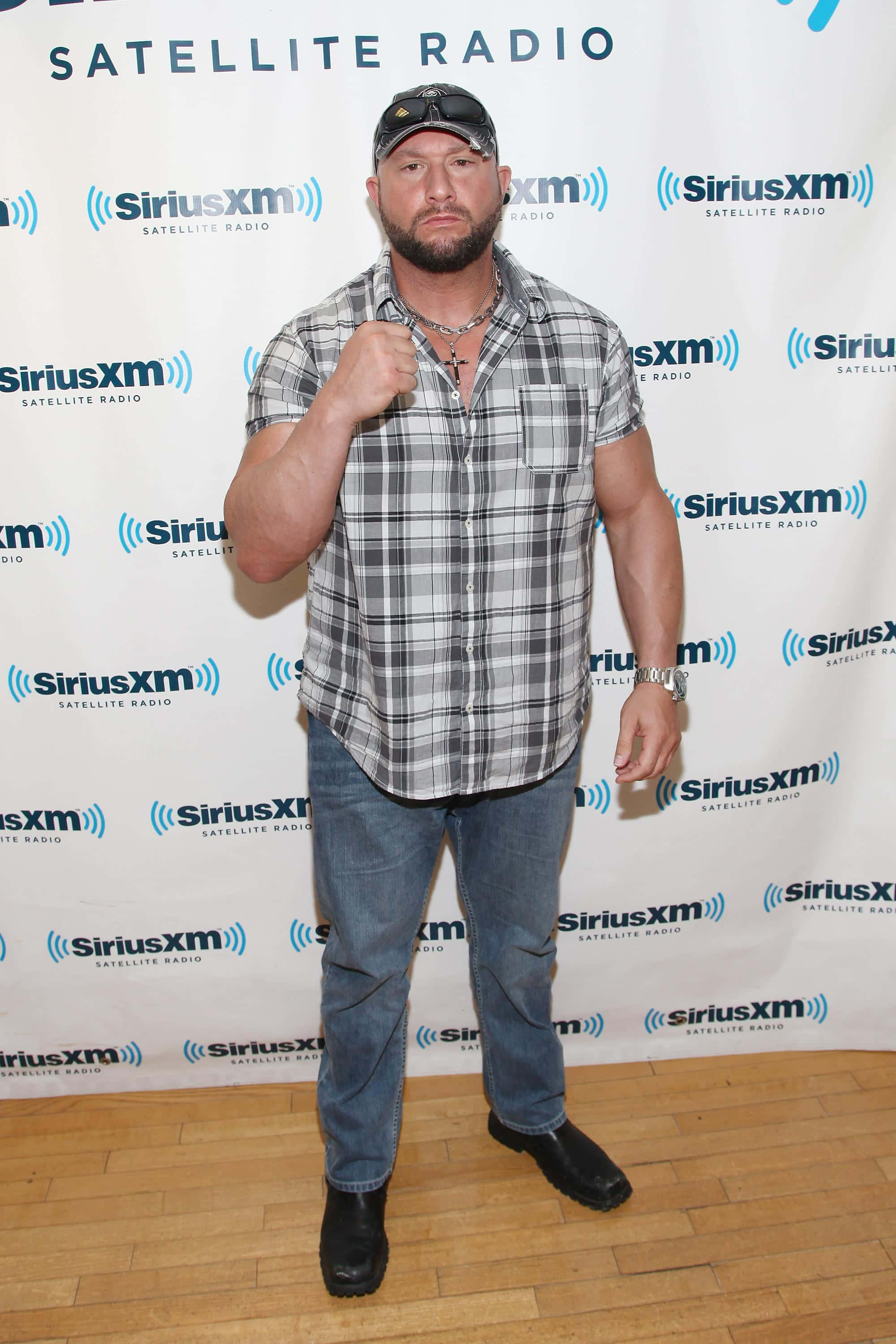 摔角 桌布 壁紙 — 一個肌肉發達的男人穿著格紋襯衫和牛仔褲，在SiriusXM品牌背景下自信地舉起拳頭擺姿勢。