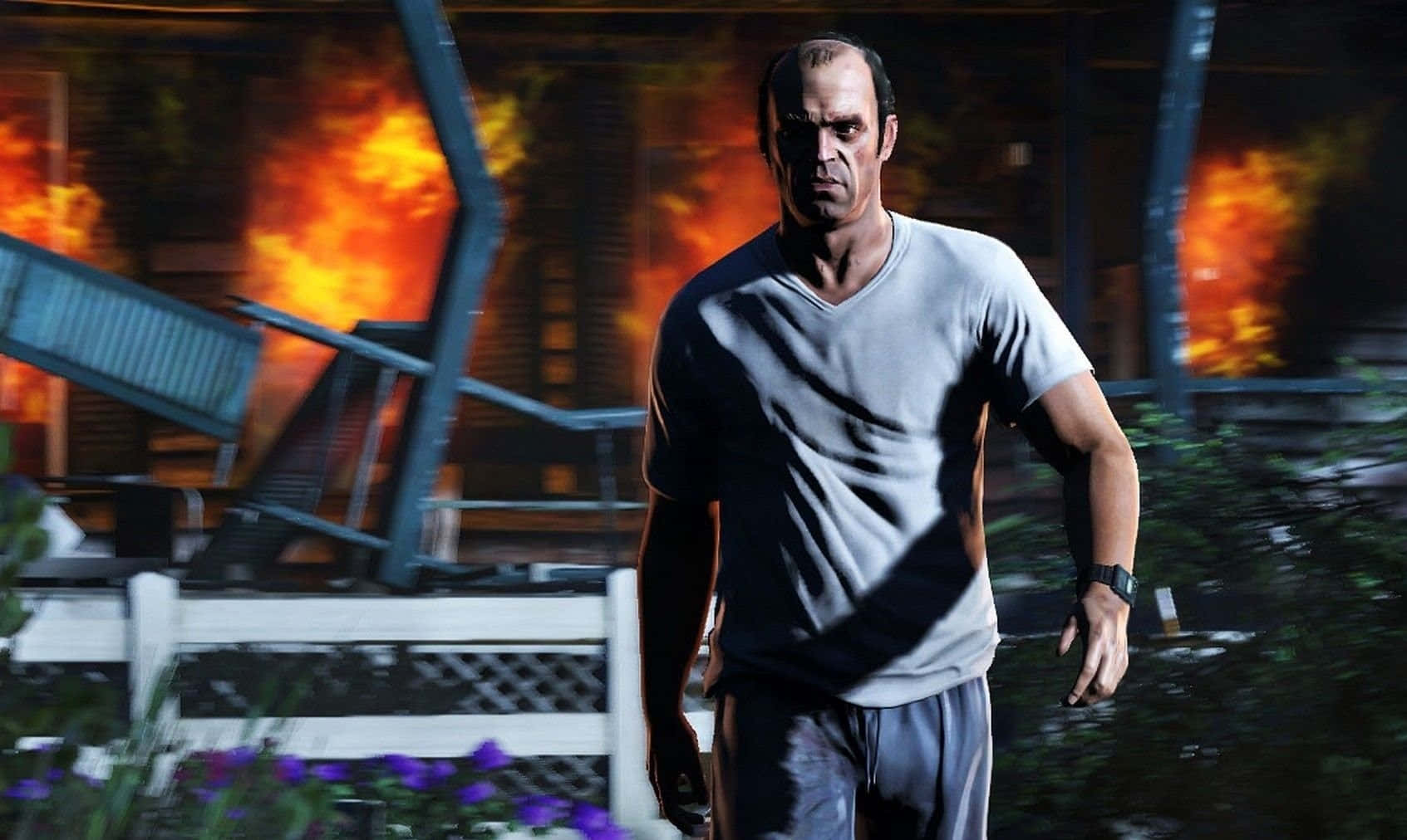 Gta 5 Desktop 桌布 壁紙 — 一個肌肉發達的男人穿著灰色T恤，面帶嚴肅表情向前走，身後在混亂的城市環境中爆發熾熱的爆炸。
