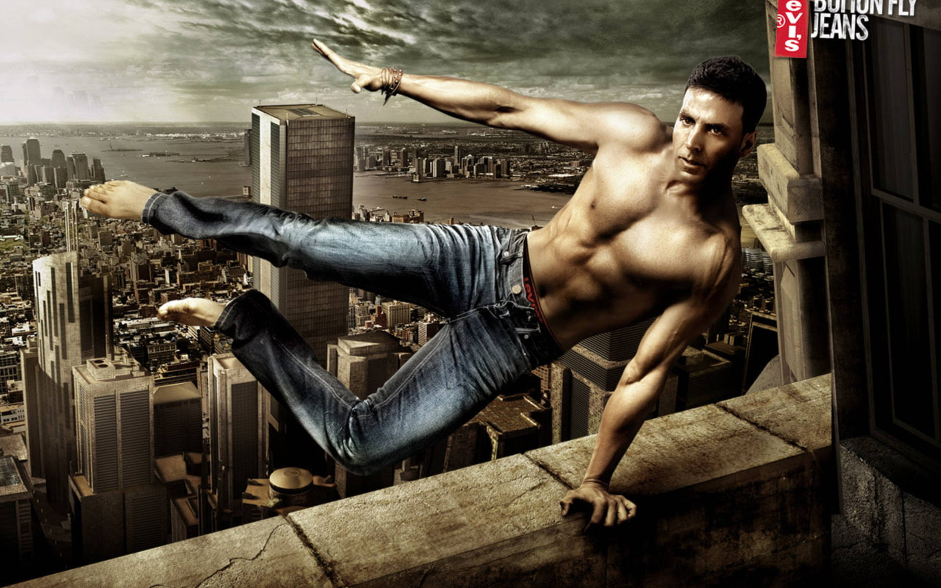Akshay Kumar 桌布 壁紙 — 一個肌肉發達的男人穿著牛仔褲，掛在摩天大樓的邊緣，俯瞰著在戲劇性的多雲天空下延伸的城市景觀。