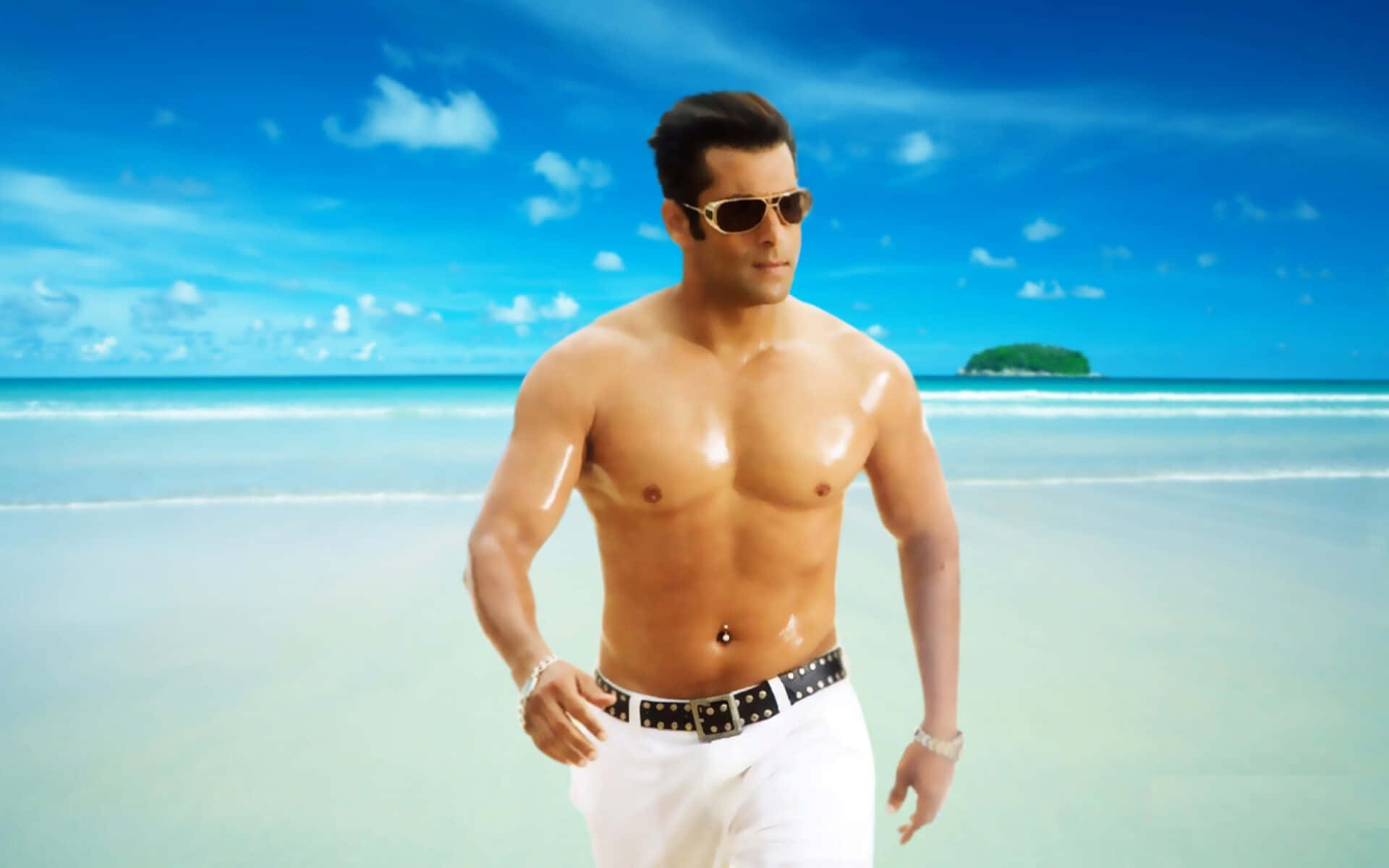Salman Khan 桌布 壁紙 — 一個肌肉發達的男人穿著白色褲子和太陽眼鏡，在陽光明媚的熱帶海灘上自信地行走，海水碧綠，遠處有島嶼，天空湛藍。