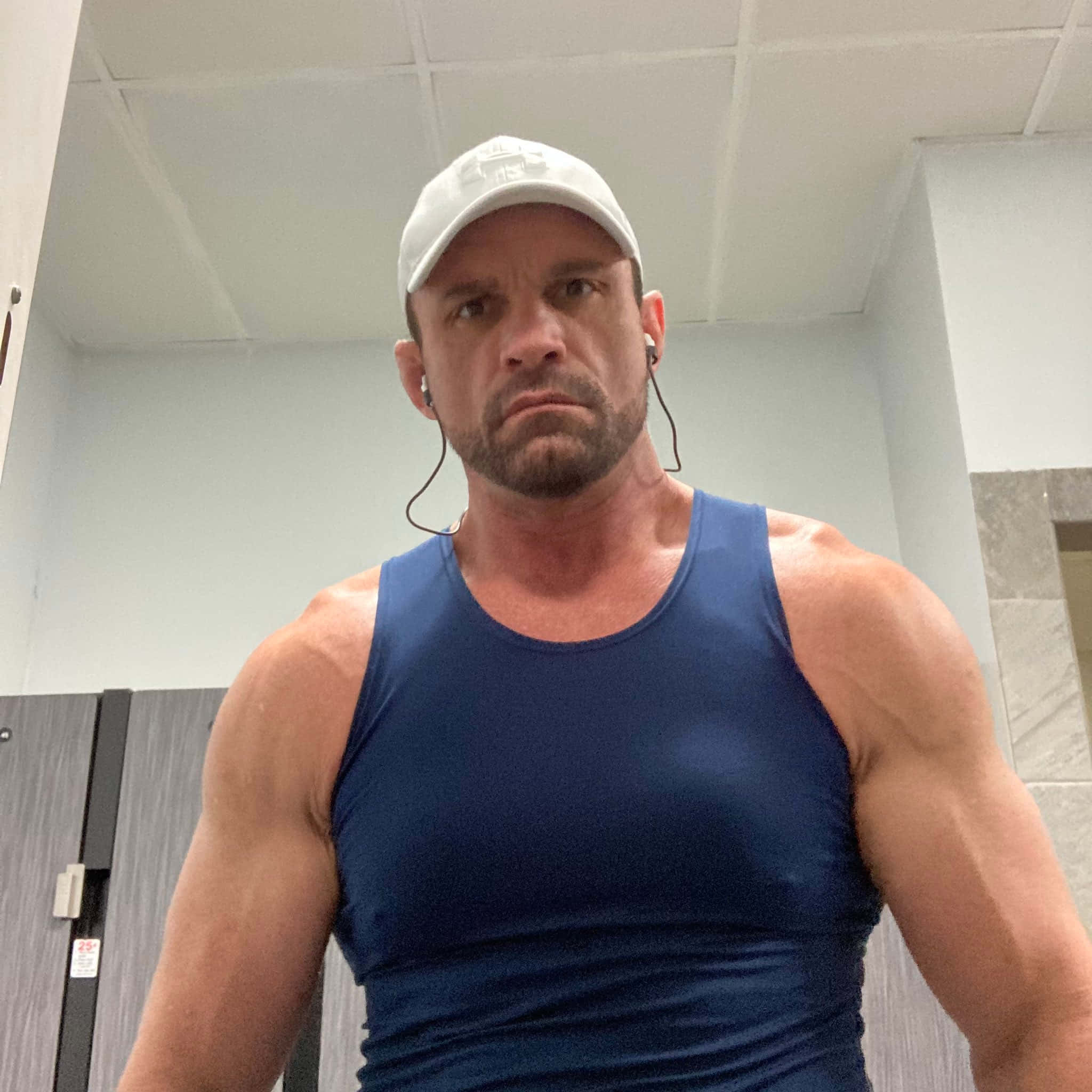 WWE 桌布 壁紙 — 一個肌肉發達的男人穿著藍色背心和白色帽子，在健身房更衣室裡凝視著鏡頭。