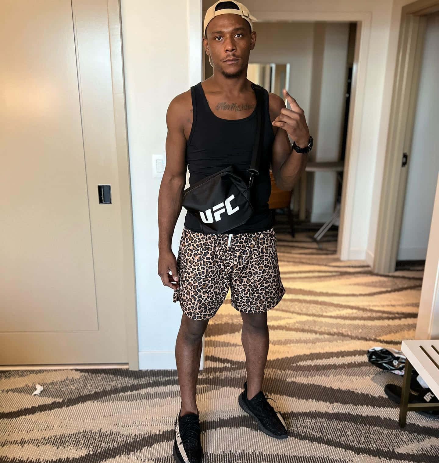 UFC 桌布 壁紙 — 一個肌肉發達的男人穿著豹紋短褲和UFC包包，自信地站在飯店走廊。