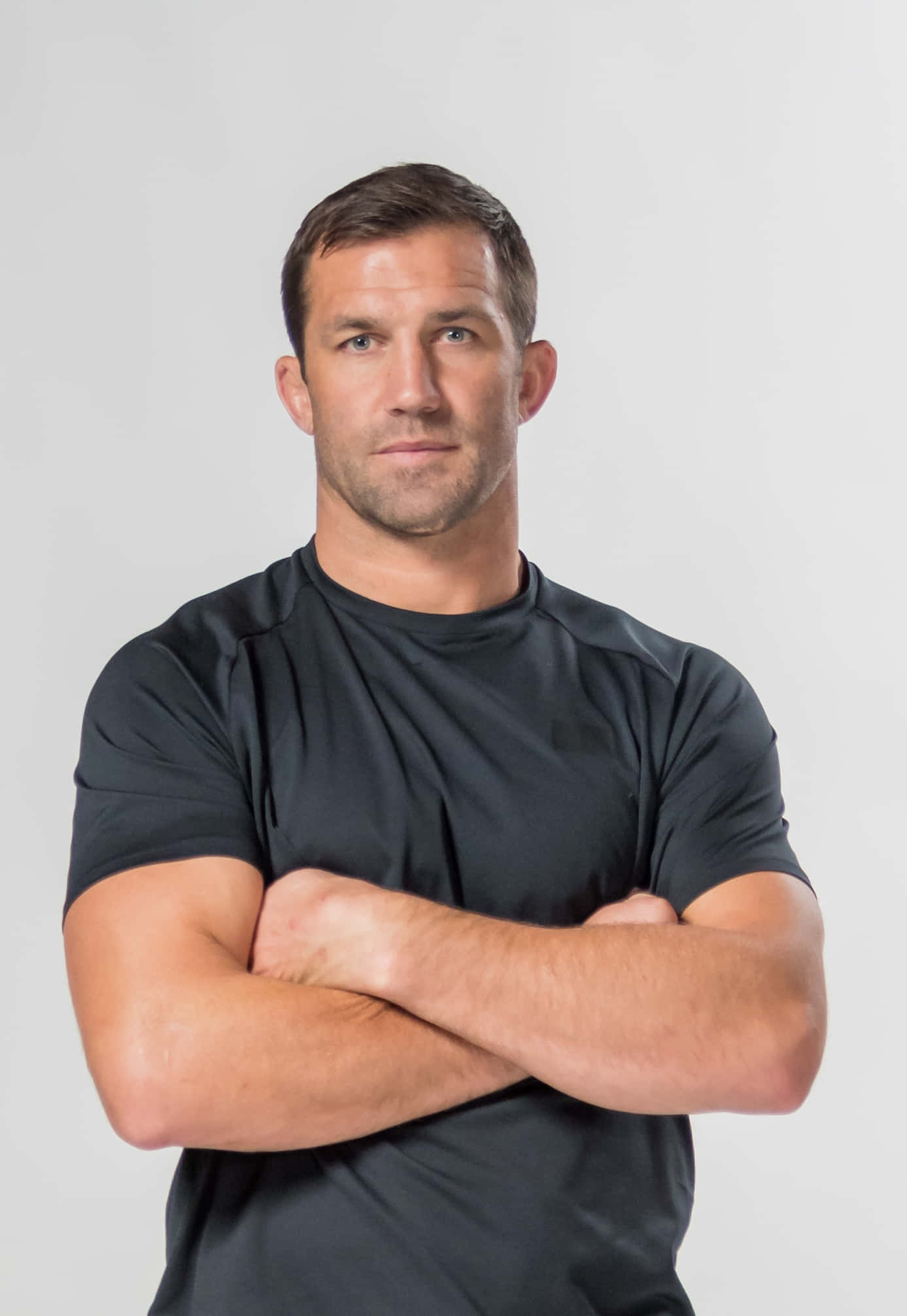 UFC 桌布 壁紙 — 一個肌肉發達的男人穿著黑色T恤，雙臂交叉，自信地站在純灰色背景前。
