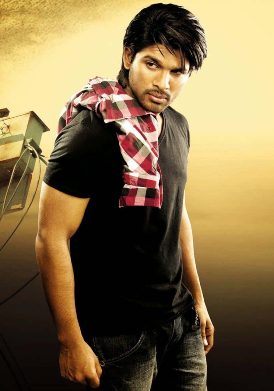 Allu Arjun 桌布 壁紙 — 一個肌肉發達的男人穿著黑色T恤和牛仔褲，肩上披著一條紅色格紋圍巾，在溫暖的金色漸層背景前自信地擺姿勢。